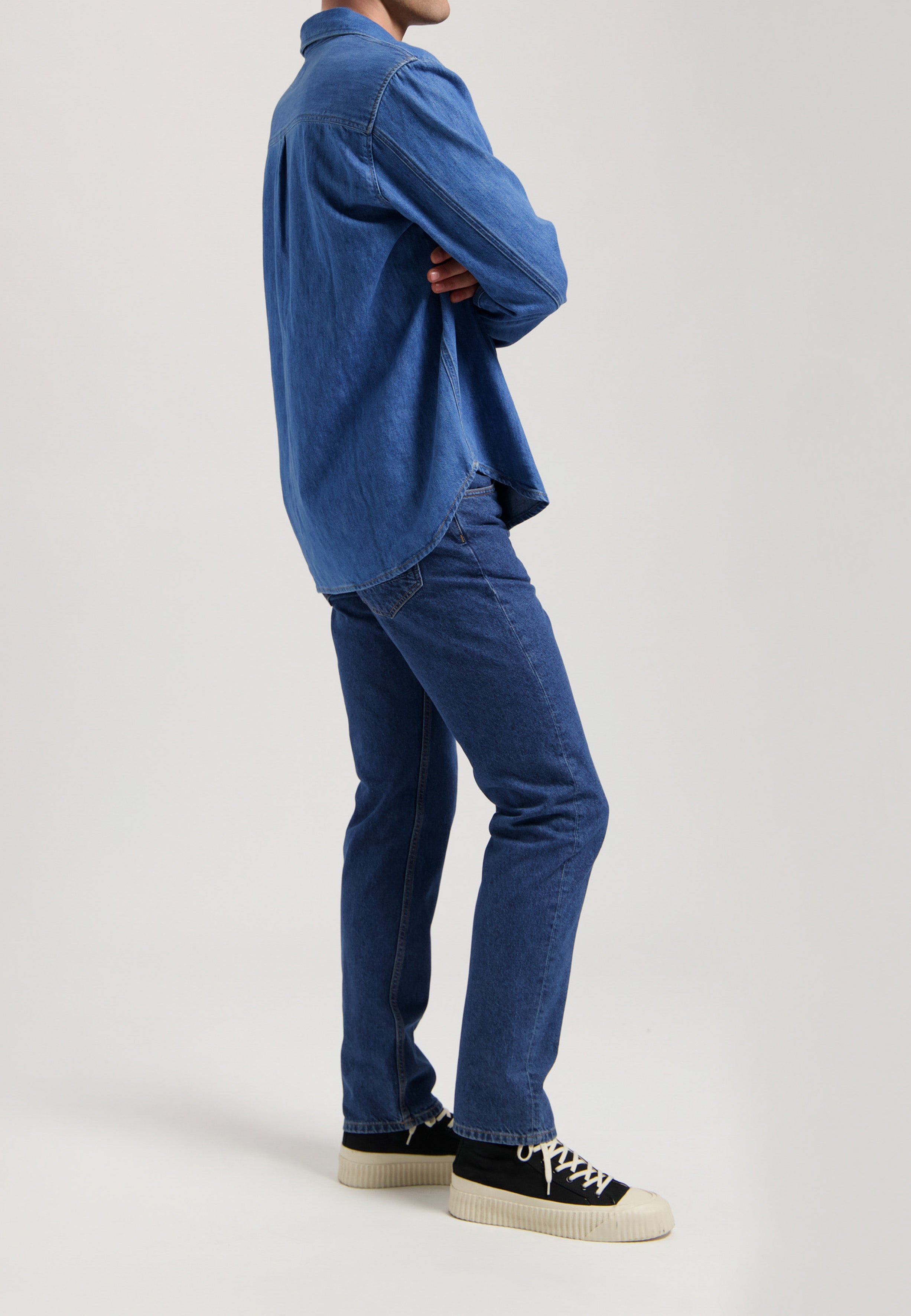 Sustainable MUD Jeans in dark denim, paired with a white long-sleeve top, emphasizing ethical fashion choices.