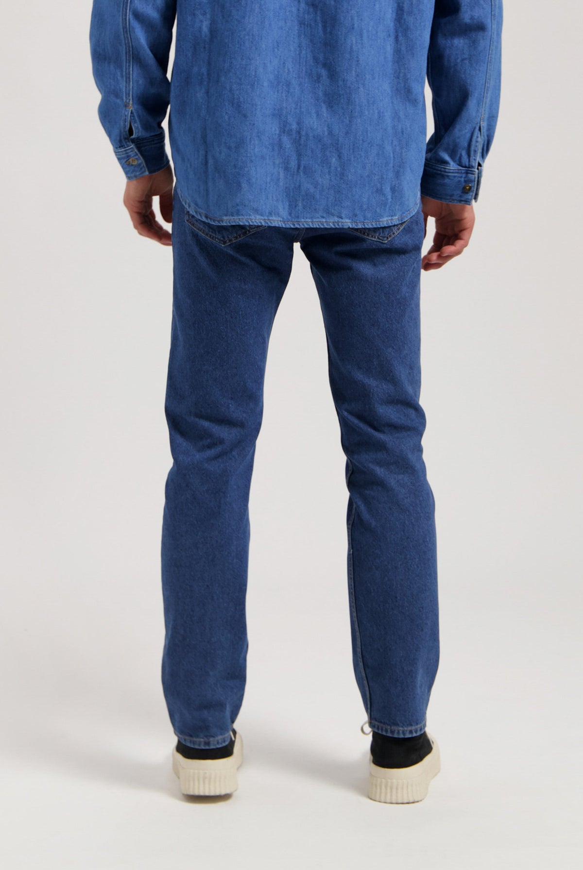 Sustainable MUD Jeans in dark denim, crafted ethically from organic cotton, shown with a white shirt and black shoes.