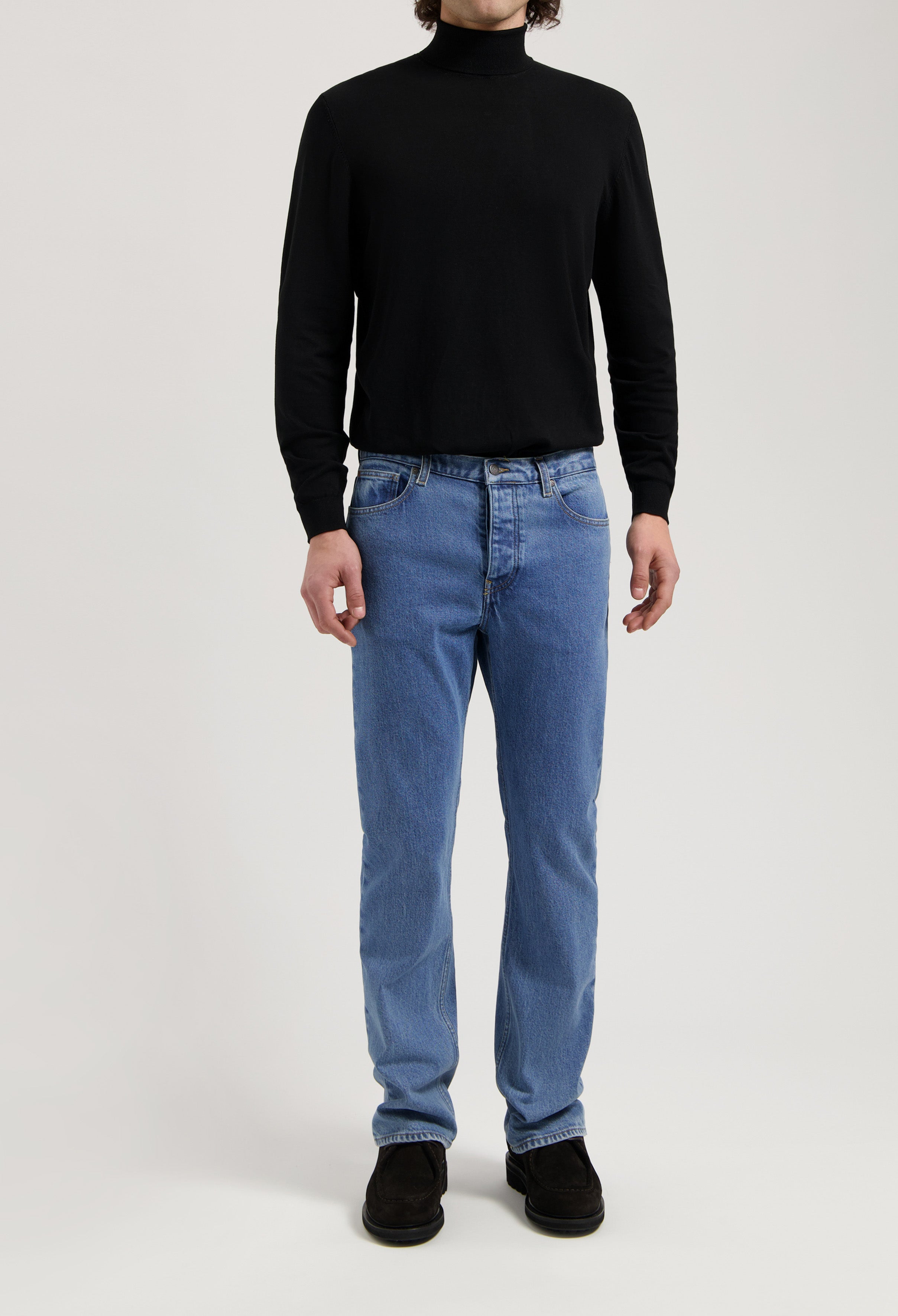 Sustainable MUD Jeans made from organic denim, featuring classic blue straight-fit, paired with a black turtleneck.