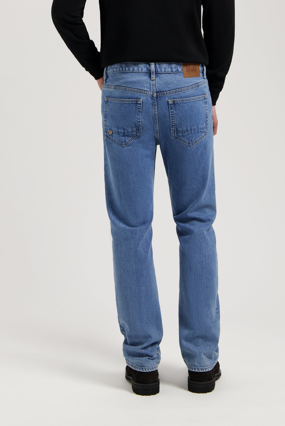 Sustainable MUD Jeans in light blue denim, featuring a classic fit with ethical craftsmanship, paired with black shoes.