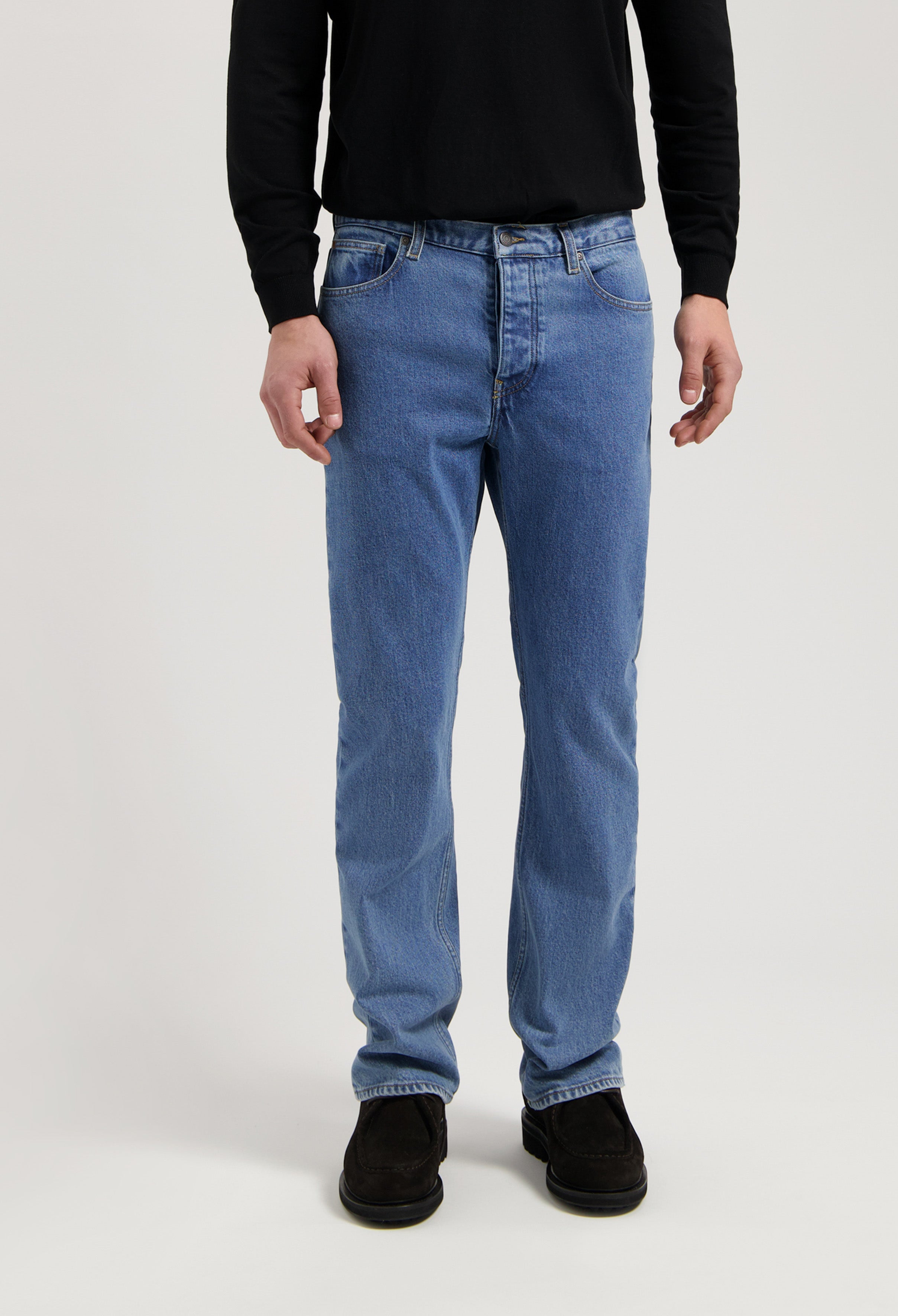 Sustainable Mud Jeans in classic blue denim, ethically made, featuring a straight fit, paired with a black long-sleeve shirt.