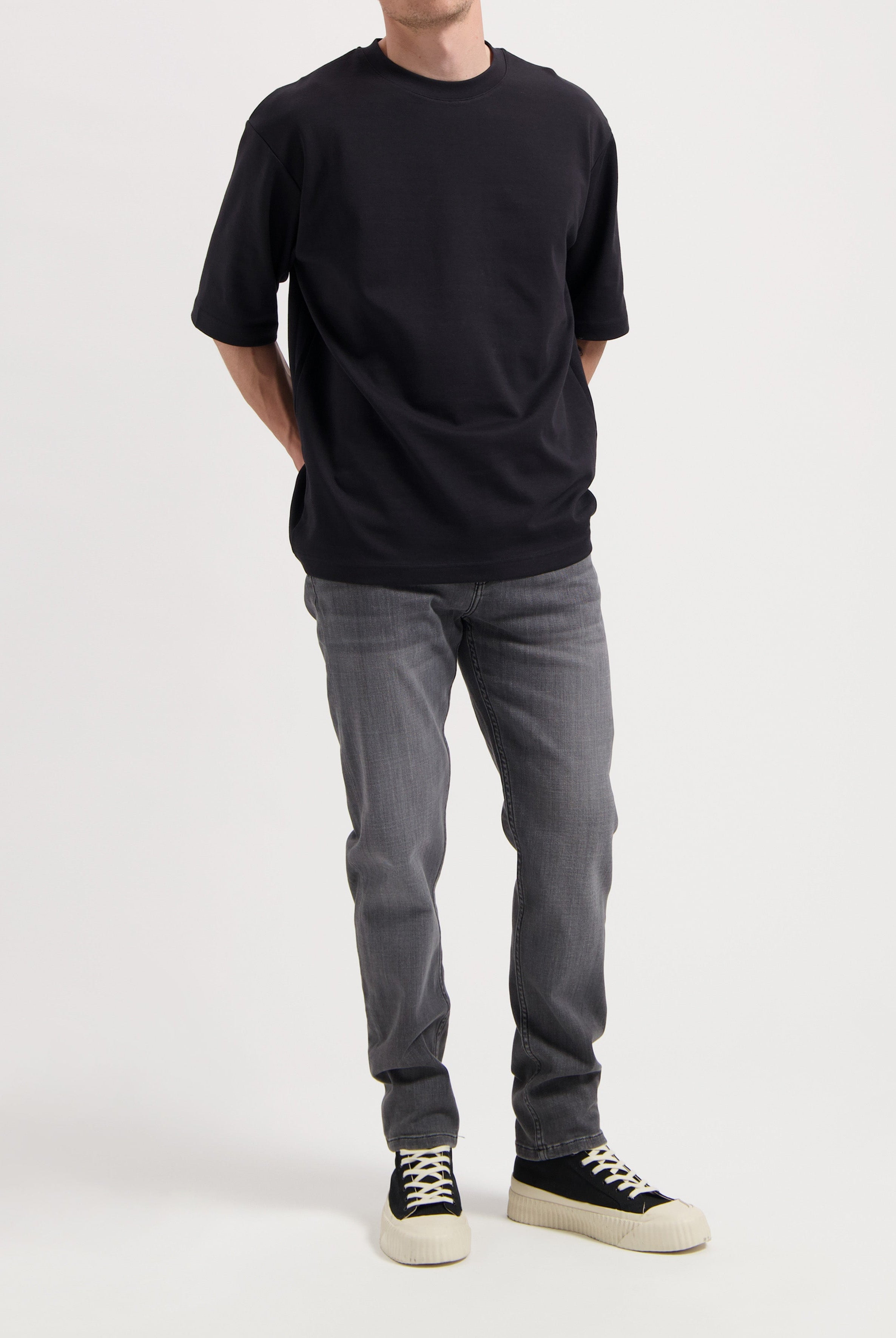 Sustainable MUD Jeans in dark blue denim, crafted from organic cotton, worn with a gray tee and white sneakers.