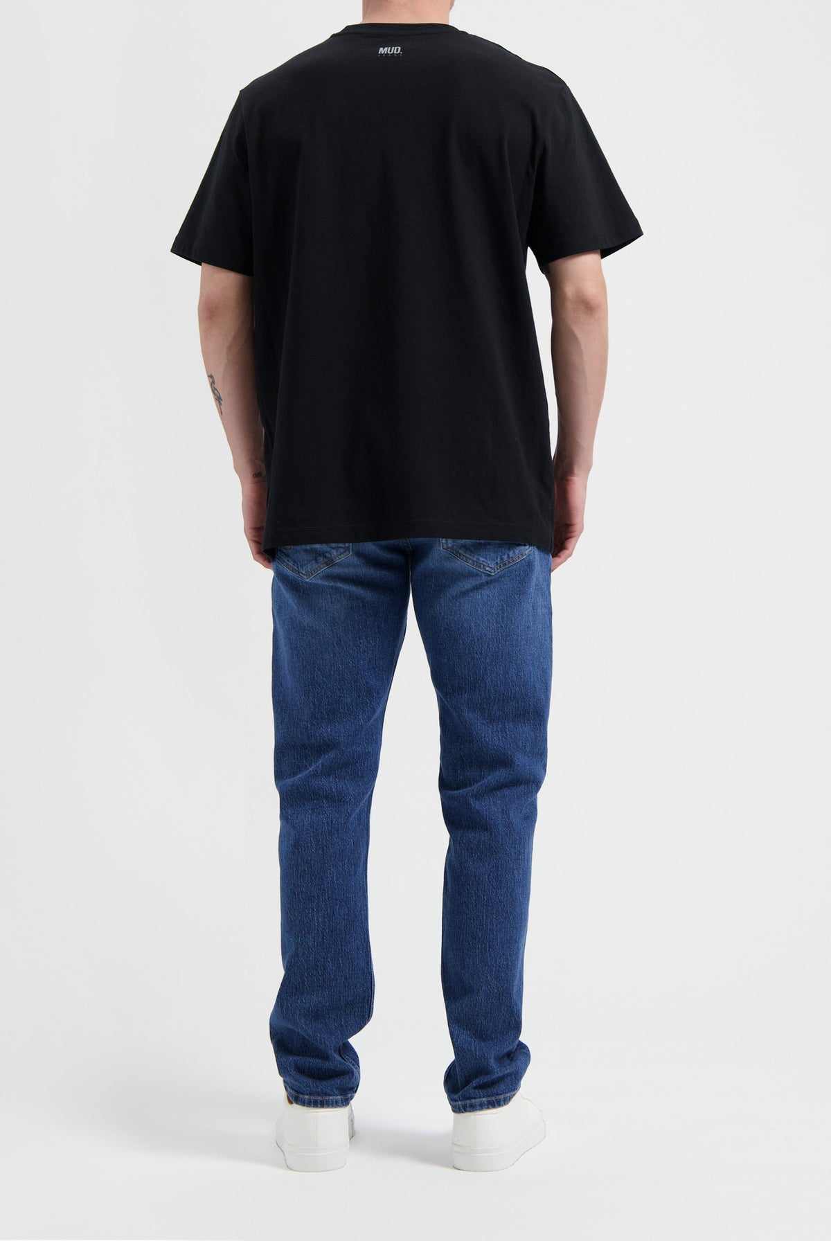 Sustainable MUD Jeans in dark brown, crafted from ethical materials, paired with a white t-shirt and sneakers.