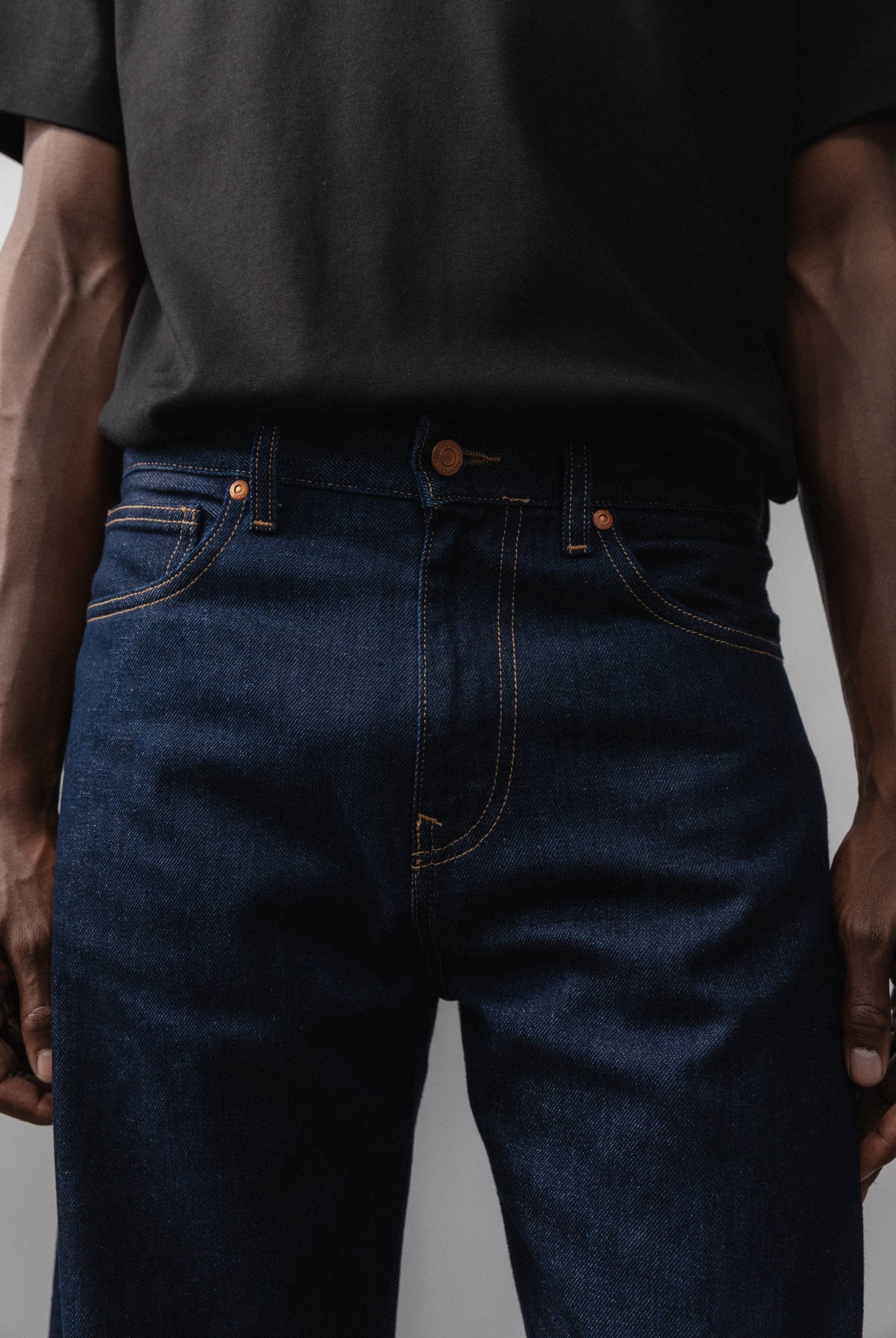 Sustainable MUD Jeans in black denim, featuring an ethical design, paired with a soft gray sweater and white sneakers.