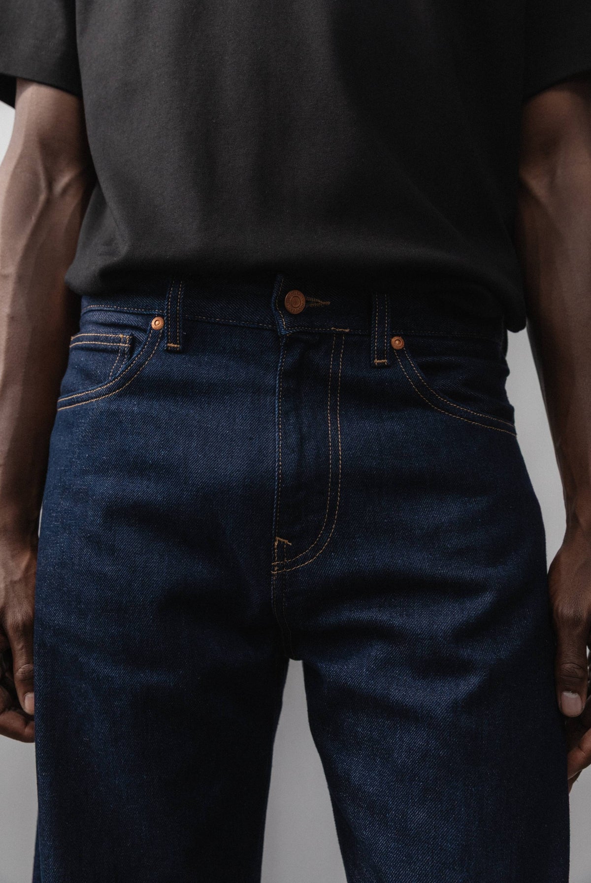 Sustainable MUD Jeans in black denim, featuring an ethical design, paired with a soft gray sweater and white sneakers.