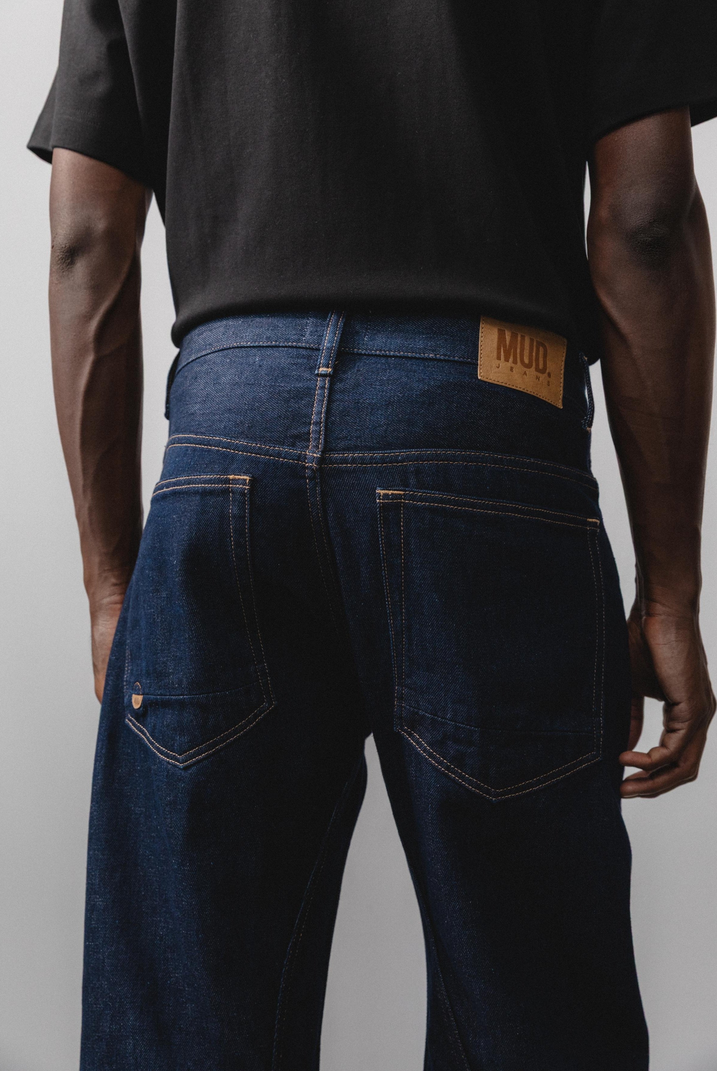 Sustainable MUD Jeans in black denim, crafted from organic cotton, worn with a light gray sweater and white sneakers.