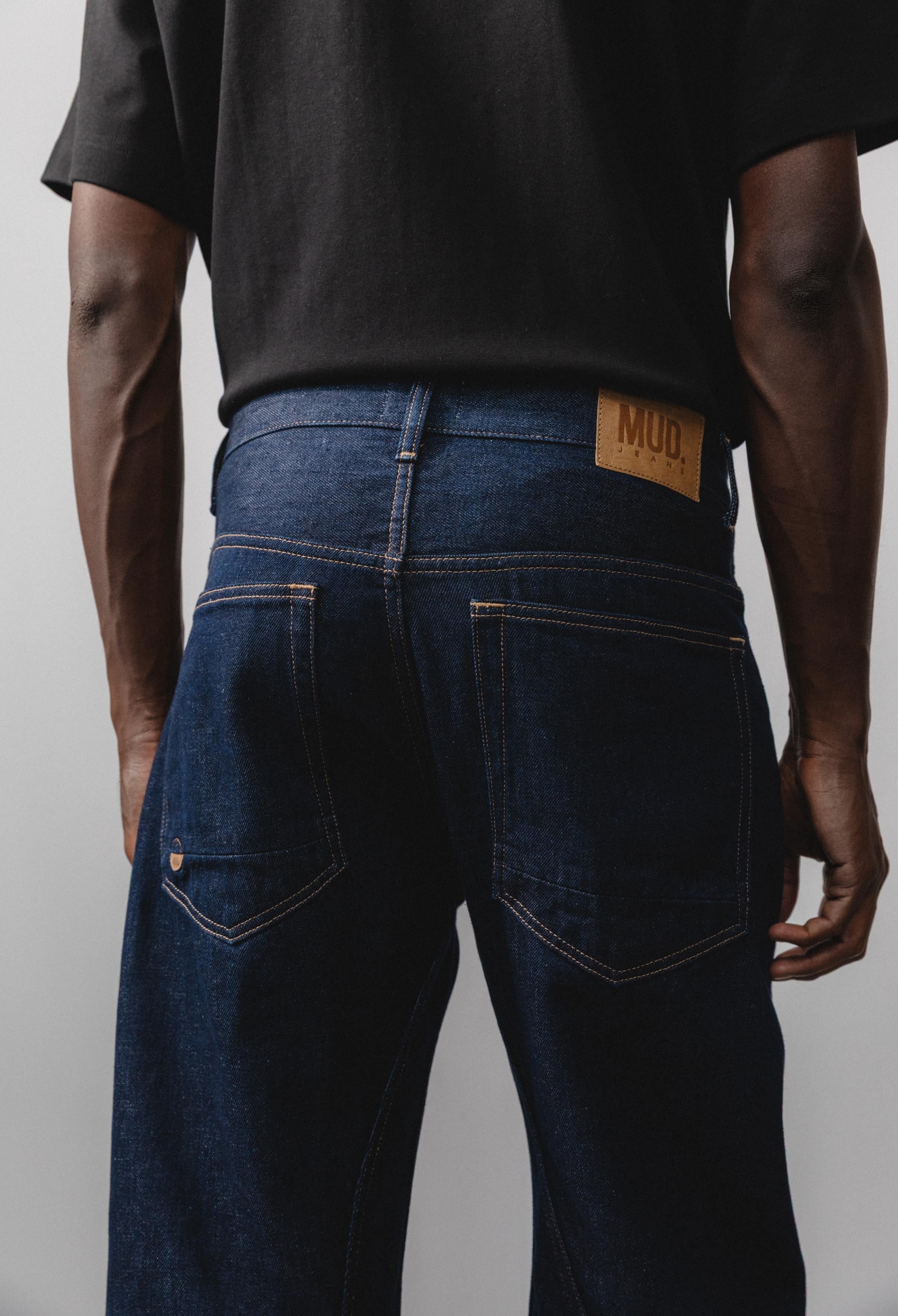 Sustainable MUD Jeans in black denim, crafted from organic cotton, worn with a light gray sweater and white sneakers.