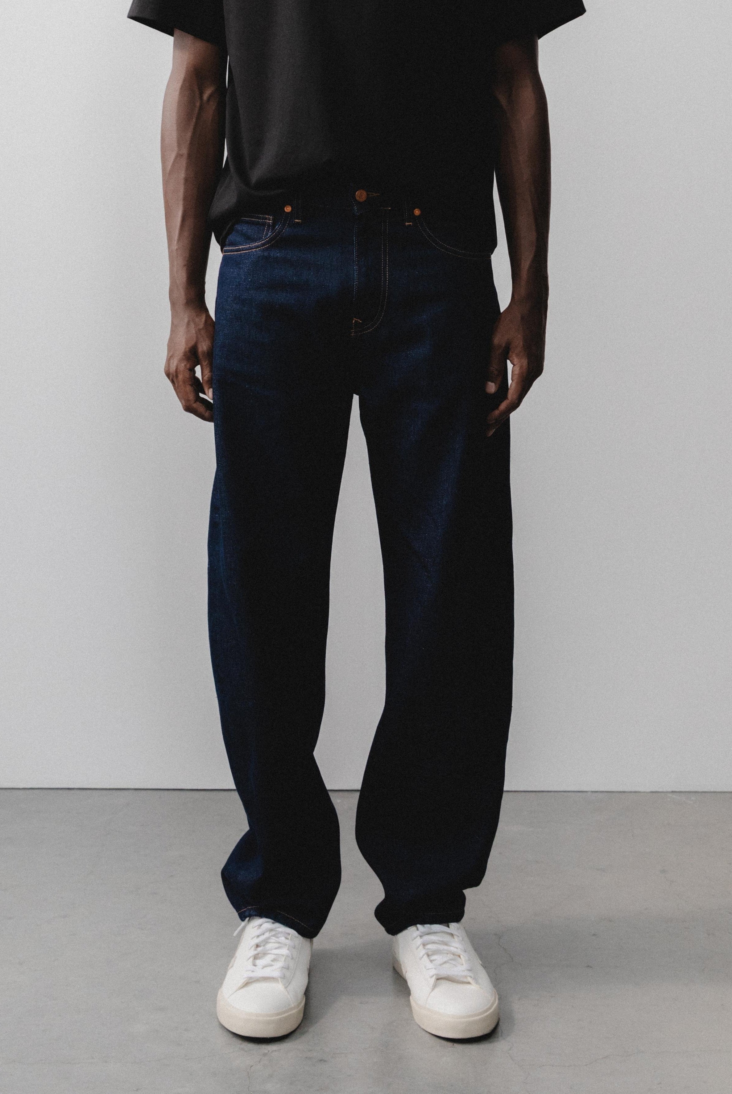 Sustainable MUD Jeans with a modern fit in deep black denim, paired with a casual gray sweater and white sneakers.