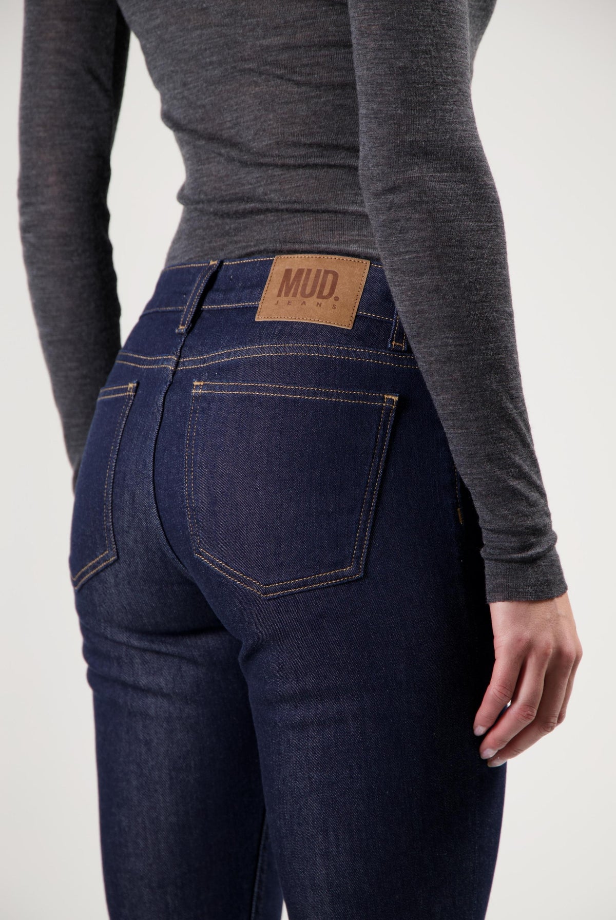 Dark blue MUD Jeans made from organic cotton, showing the back view worn with a fitted long-sleeve gray top.