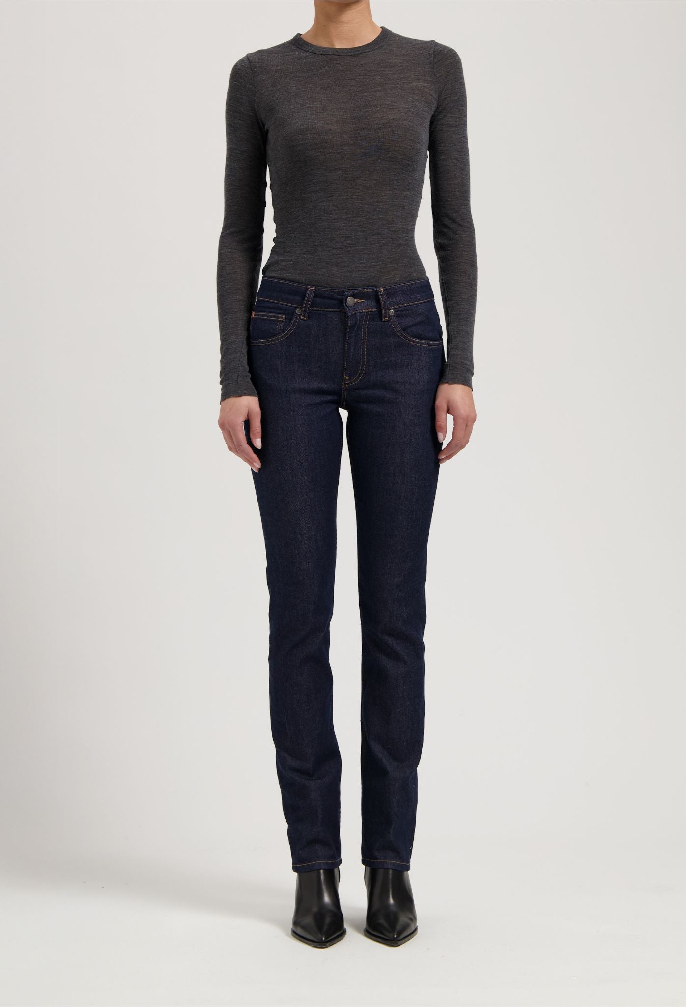 Dark blue slim-fit denim jeans paired with a long-sleeve gray top and black pointed-toe ankle boots.