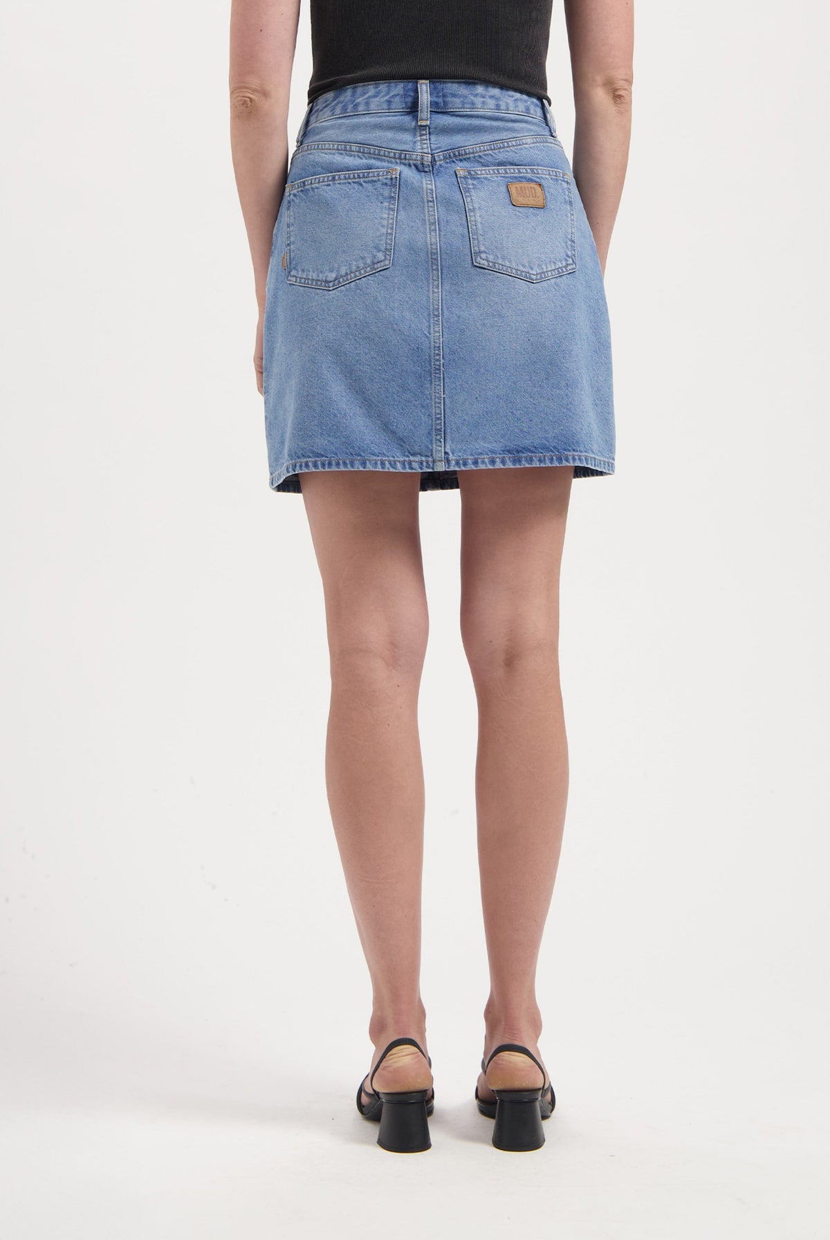 Back view of a light blue denim mini skirt with patch pockets, paired with a black sleeveless top and black heels.