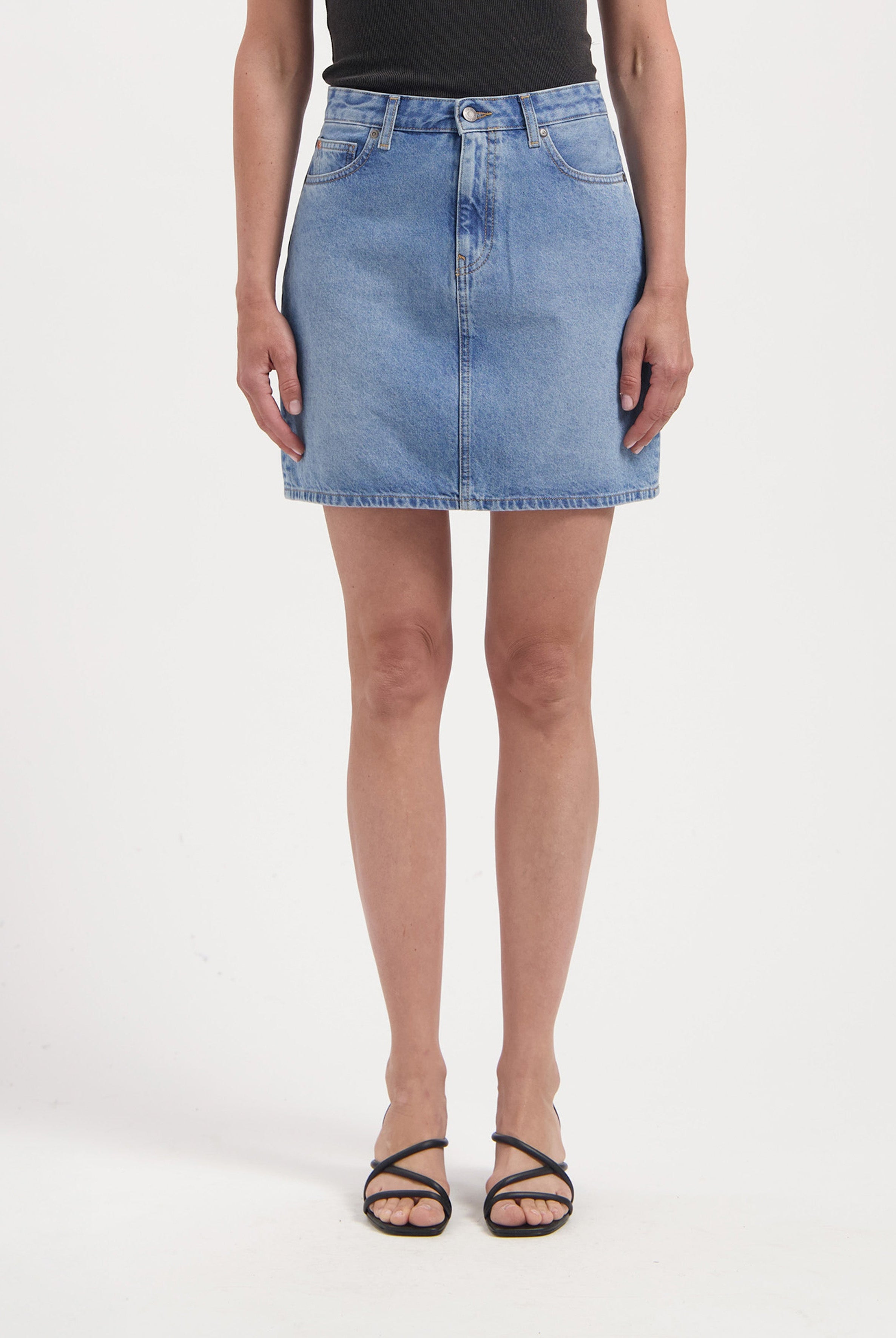 Light blue denim skirt in classic A-line style, paired with a black sleeveless top, worn with strappy black sandals.