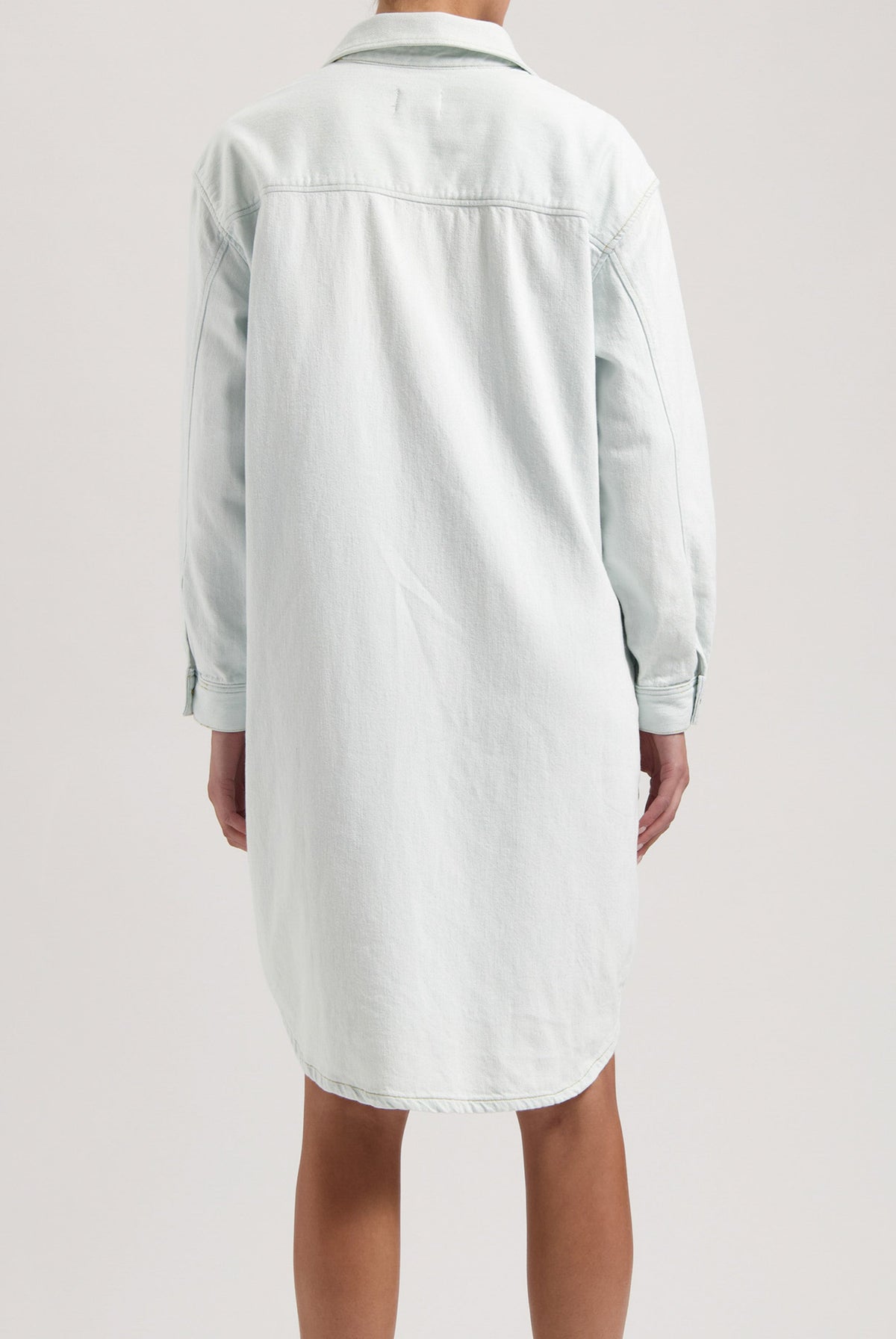 Back view of a light blue denim shirt dress showing a relaxed fit with long sleeves and classic collar design.