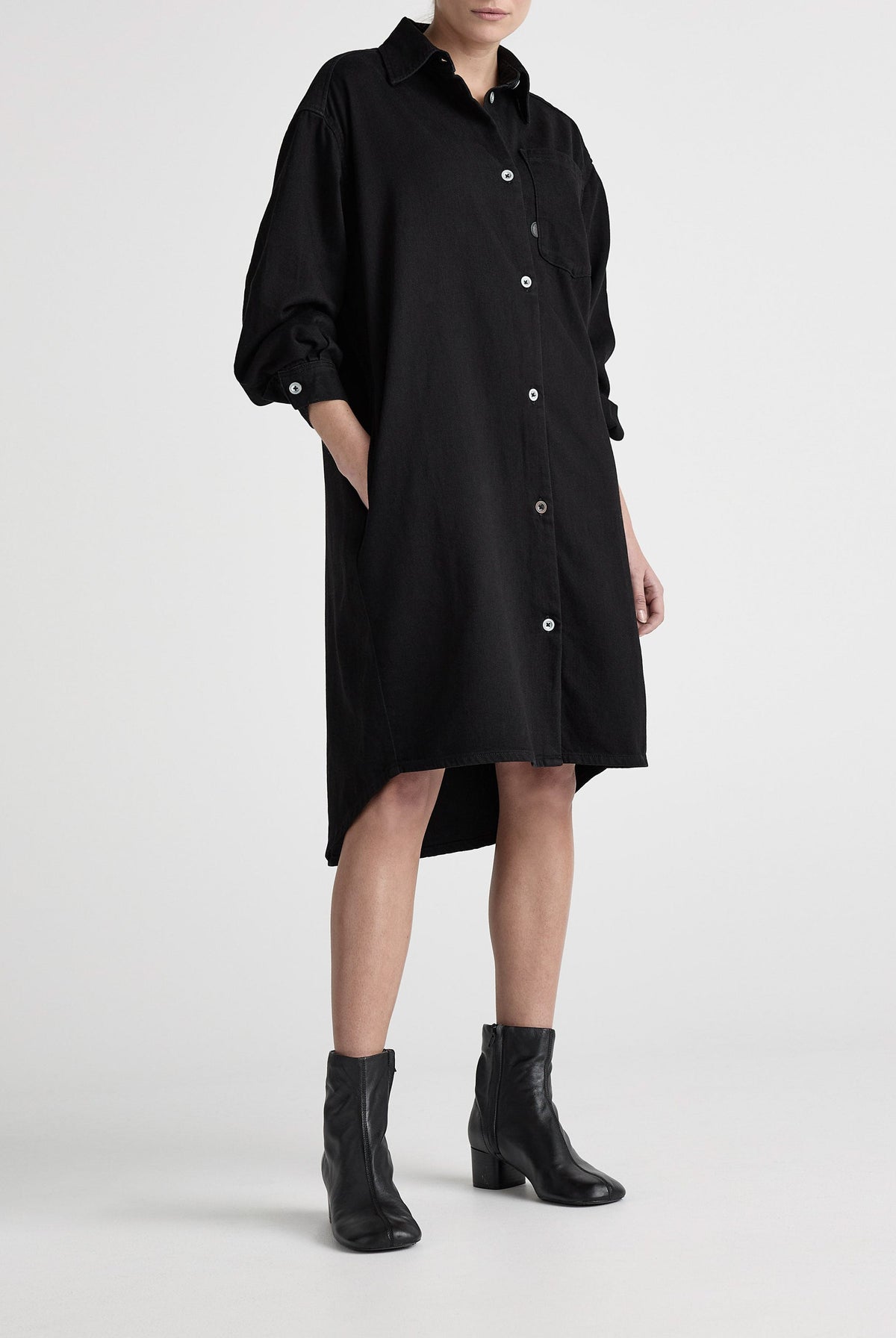 Black denim shirt dress with button-down front, featuring long sleeves and knee-length hem, paired with black ankle boots.