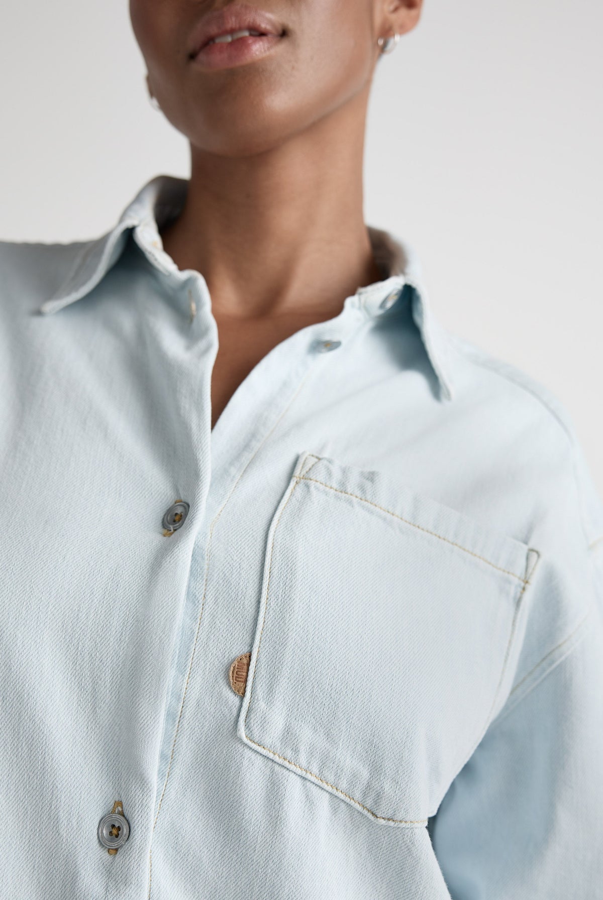 Close-up of a light blue denim shirt with button-up front and chest pocket, showcasing casual fashion style.