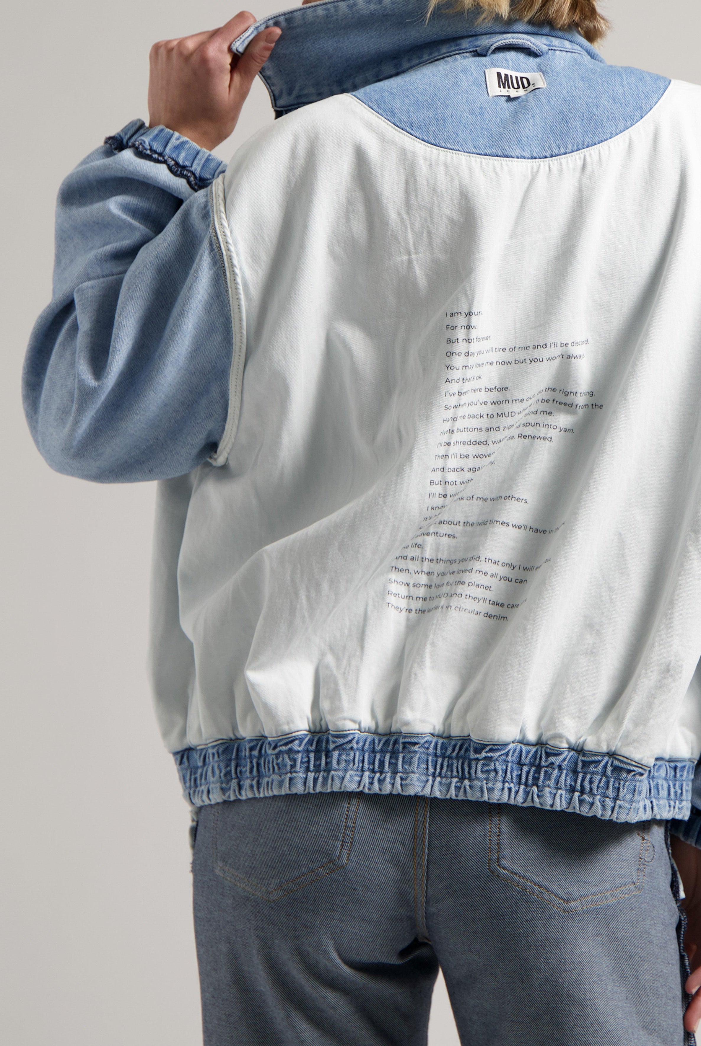 White and blue reversible denim jacket with text detail, worn over light blue jeans, highlighting sustainable MUD fashion.