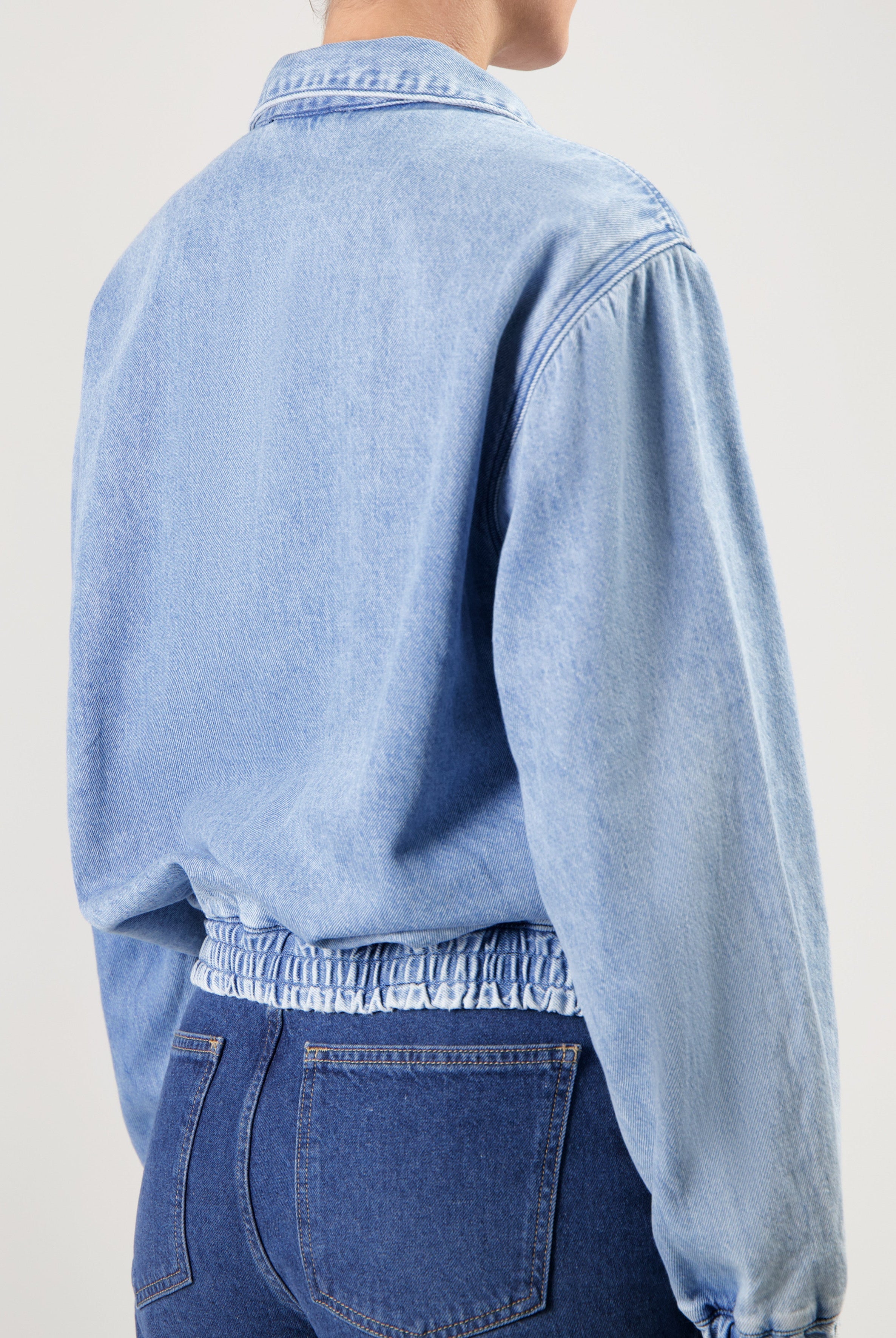 Light blue denim jacket with elastic waistband paired with dark blue high-waisted jeans, shown from the back.