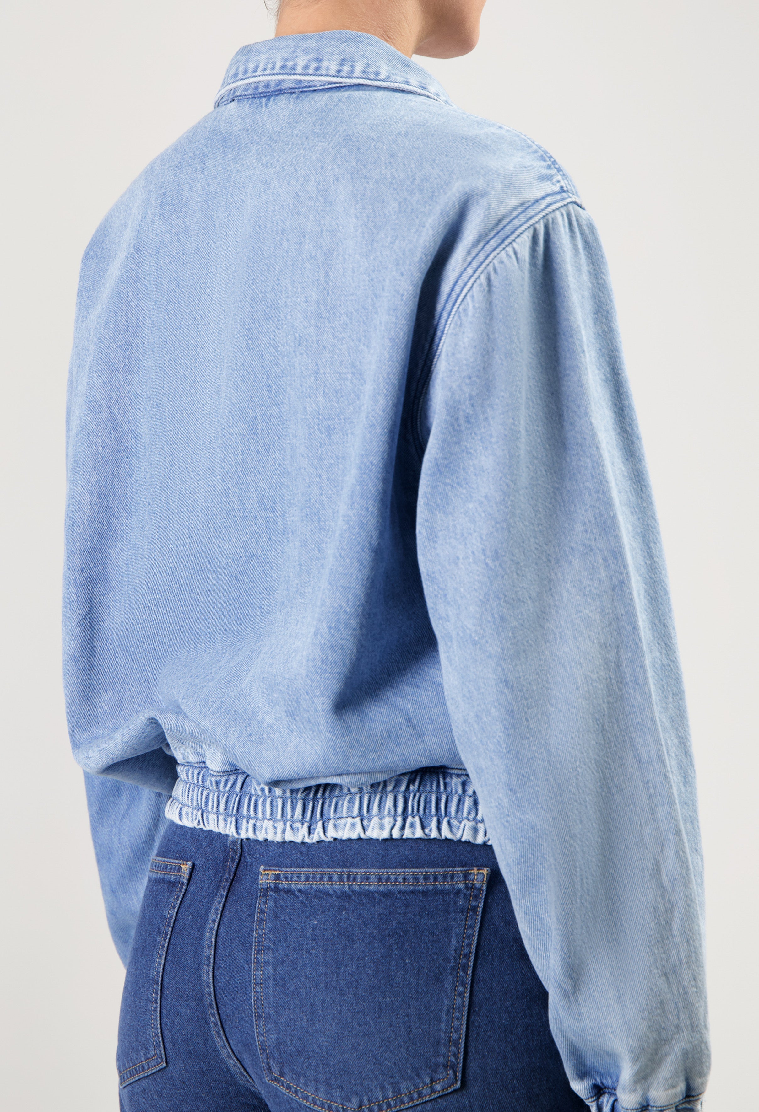 Light blue denim jacket with elastic waistband paired with dark blue high-waisted jeans, shown from the back.