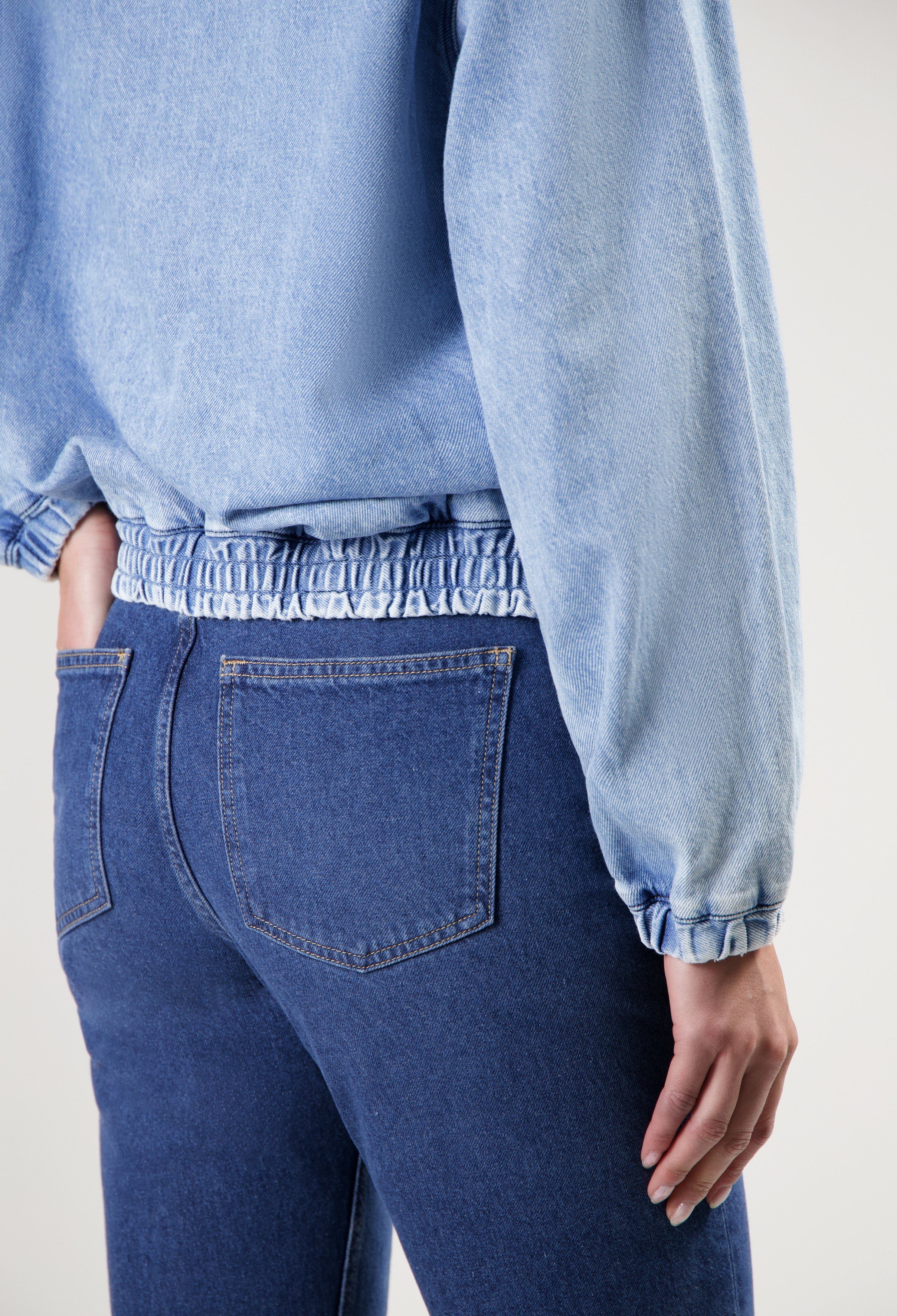 Close-up of person wearing fitted blue denim jeans paired with a light blue denim jacket, highlighting elastic waistband.