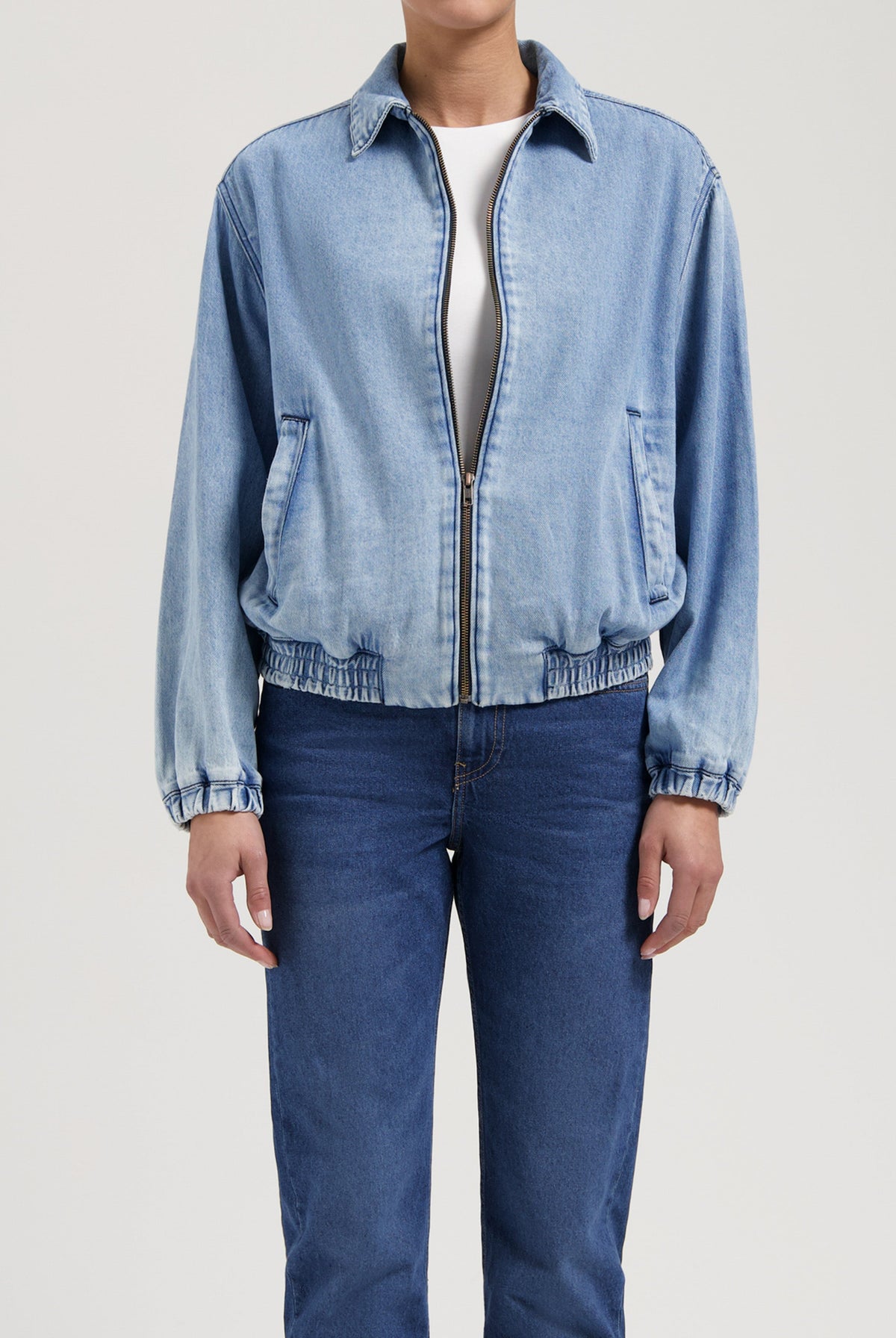 Light blue denim jacket with elastic cuffs paired with classic medium-wash jeans, showcasing casual, relaxed fit fashion.