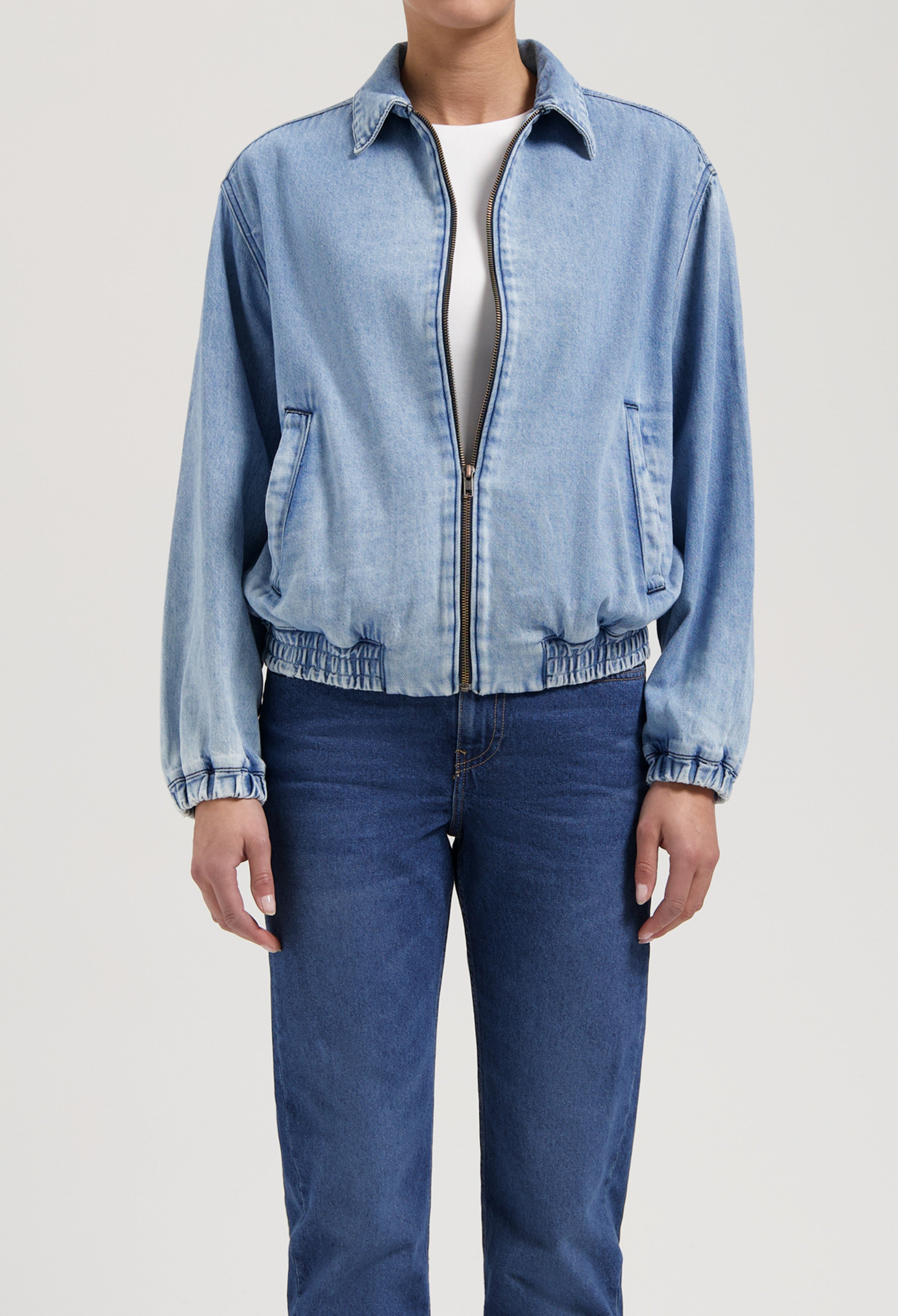 Light blue denim jacket with elastic cuffs paired with classic medium-wash jeans, showcasing casual, relaxed fit fashion.