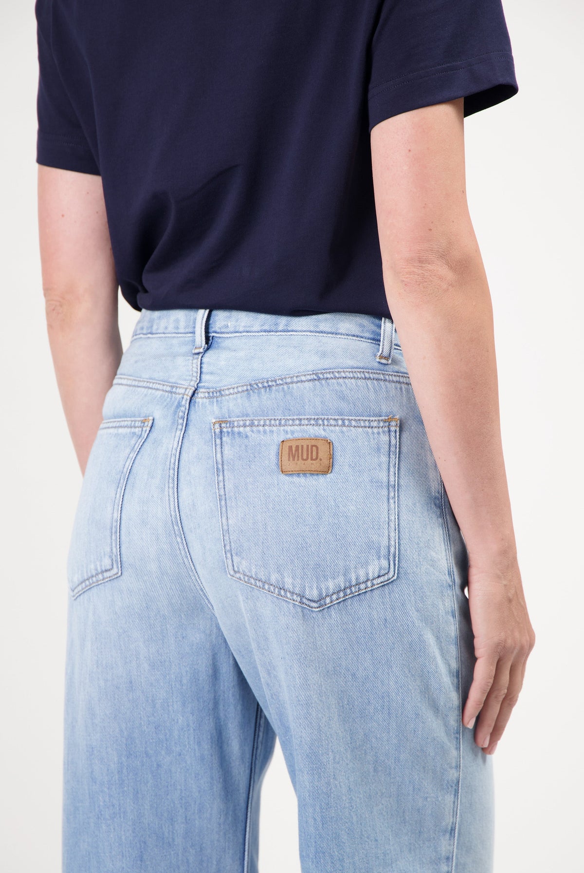 Light blue sustainable MUD Jeans showcasing the back pocket and logo detail, worn with a dark navy short-sleeve top.