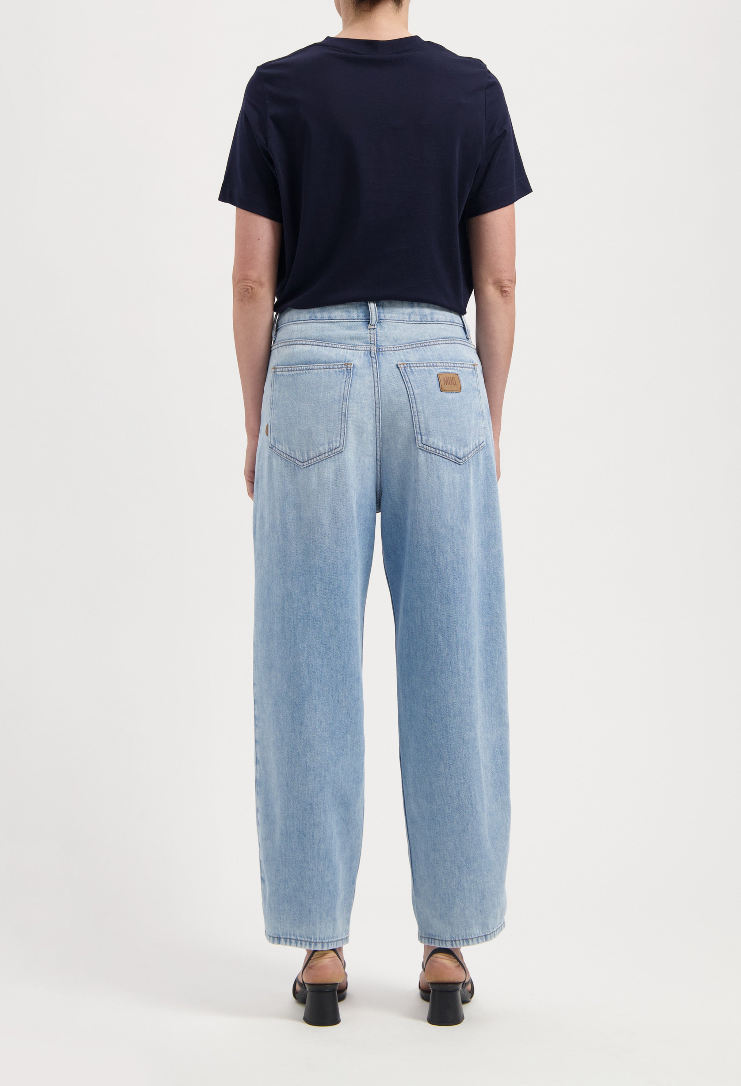 Light blue, wide-leg denim jeans with back pockets, styled with a short-sleeve navy top and open-toe black heels.