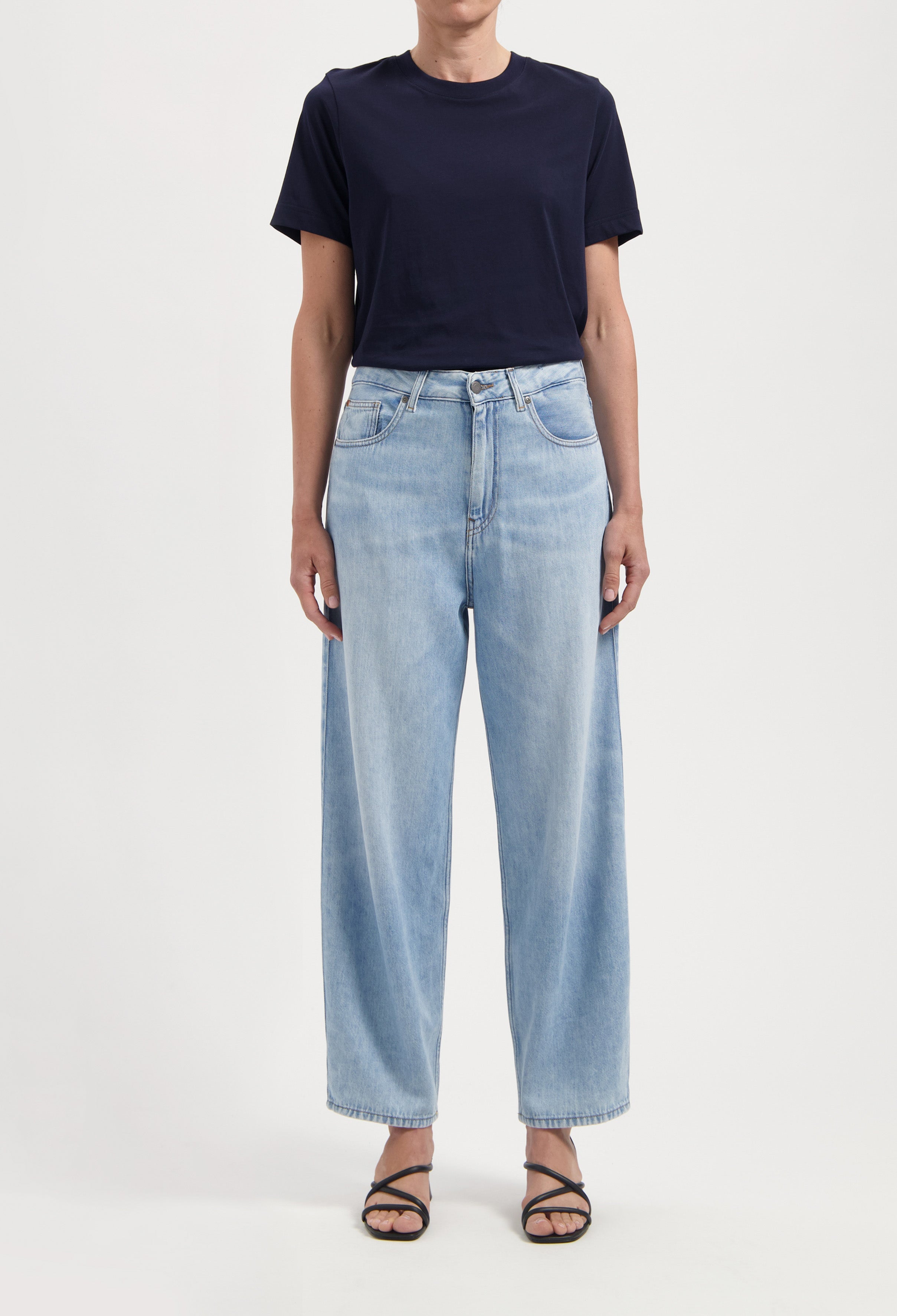 Light blue high-waisted jeans with a relaxed fit, paired with a simple black t-shirt and strappy sandals against a neutral background.