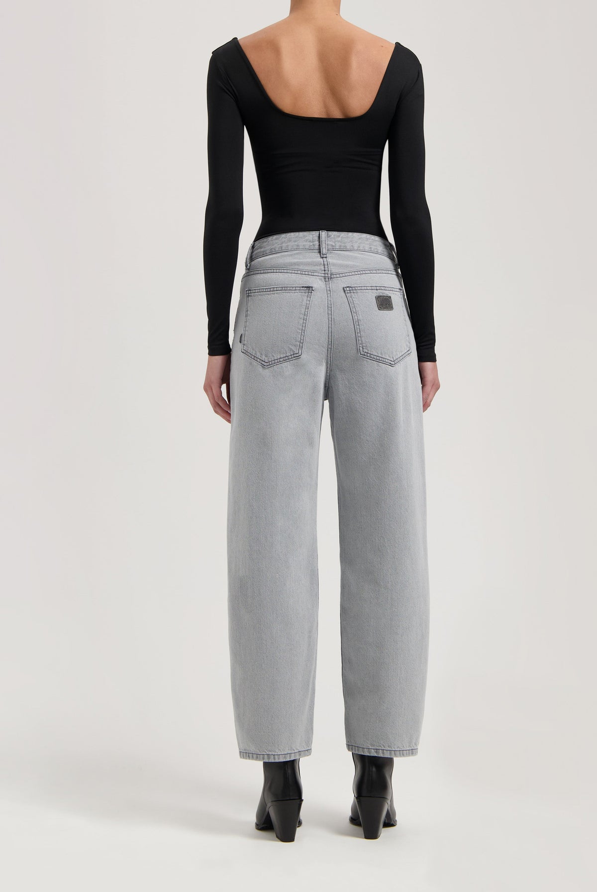 Wide-leg light gray denim jeans paired with a black long-sleeve backless top, styled with black ankle boots.