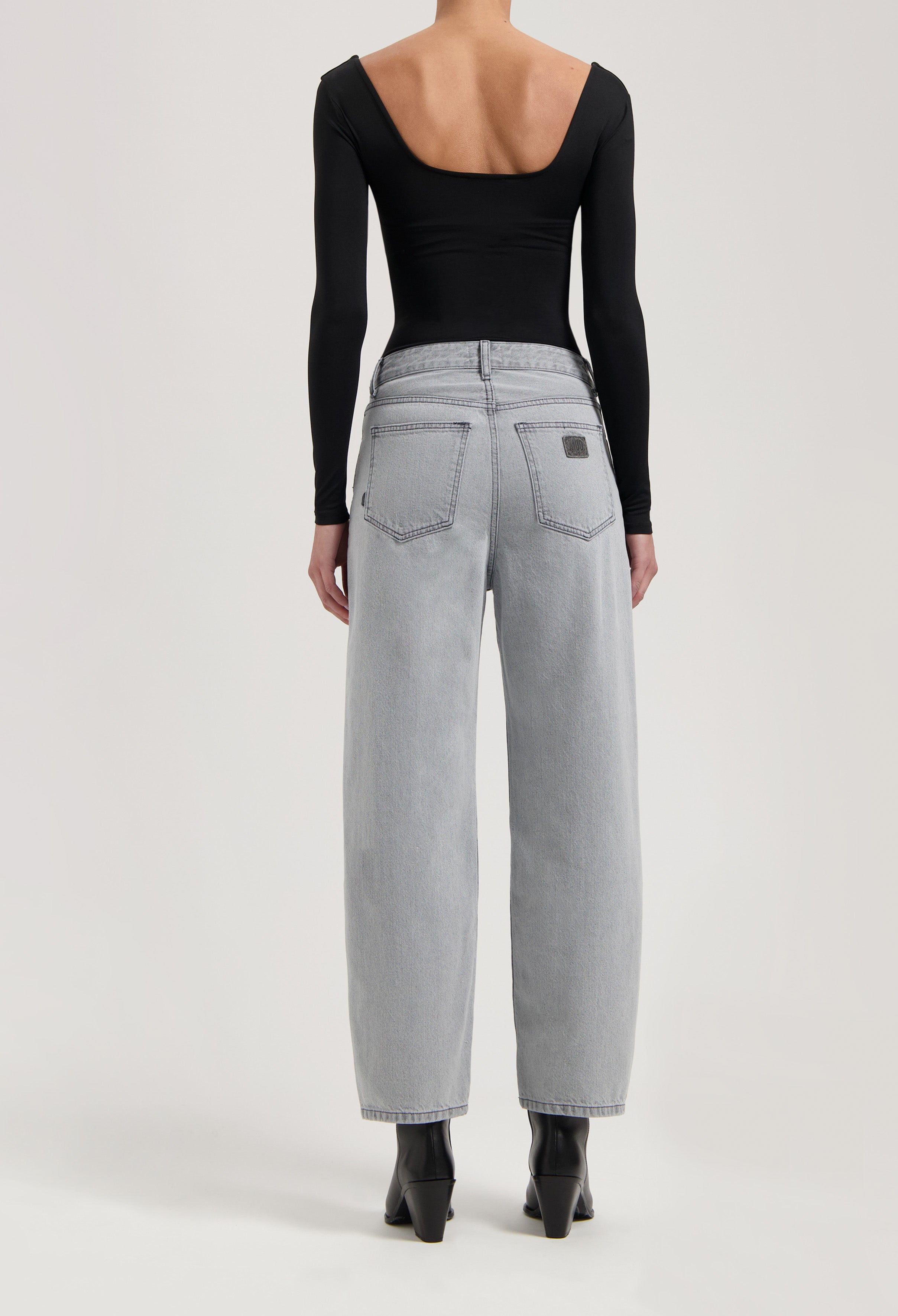 Wide-leg light gray denim jeans paired with a black long-sleeve backless top, styled with black ankle boots.