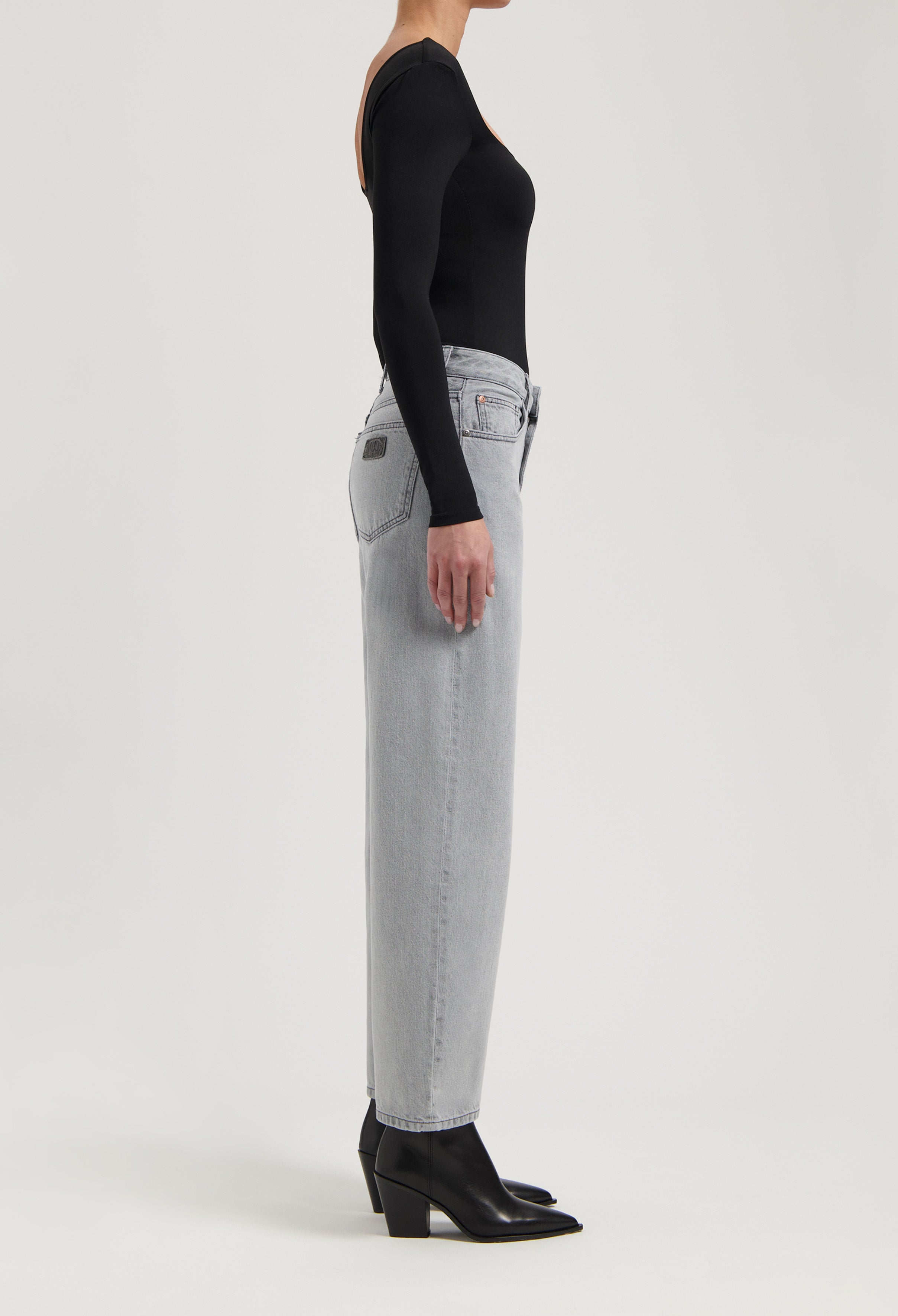 High-waisted straight-leg gray jeans made from denim, paired with a black long-sleeve top and black pointed boots.