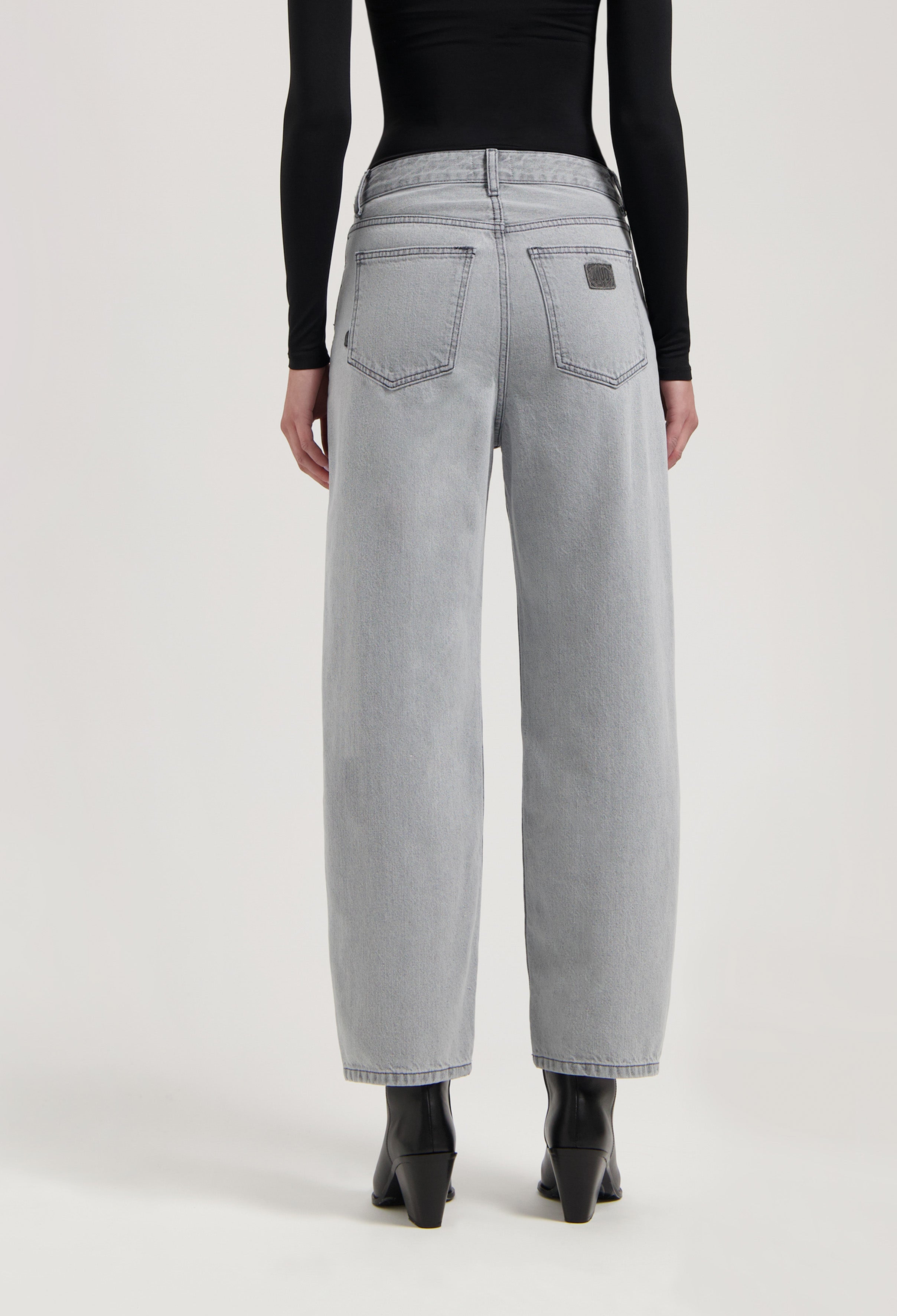 High-waisted light gray jeans with wide-leg cut, showing back view, paired with black long-sleeve top and black boots.