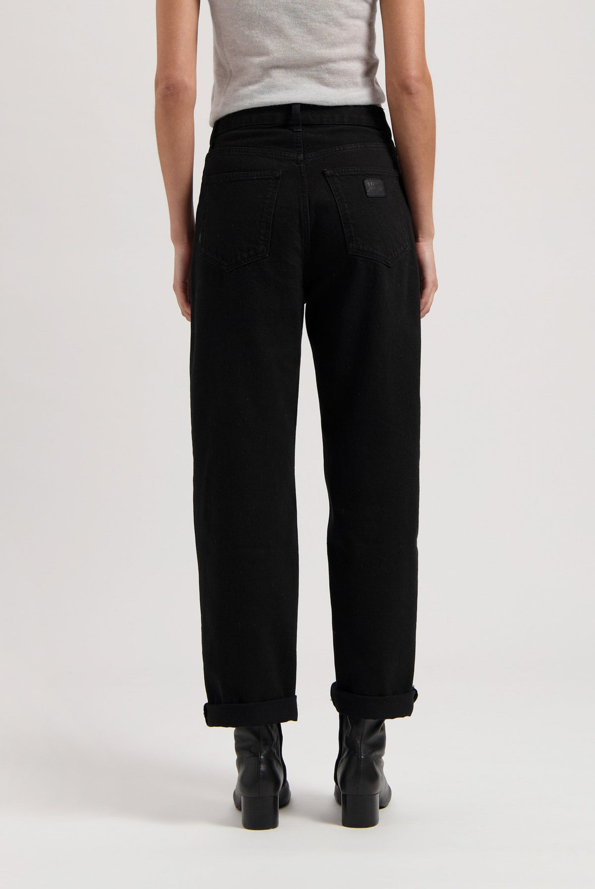 Black high-waisted jeans made of cotton, shown from the back, paired with black boots and a light gray sleeveless top.