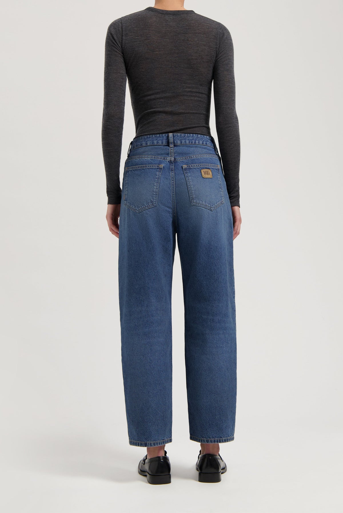 High-rise blue denim jeans made from organic cotton, worn with a fitted dark gray long-sleeve top and black loafers.