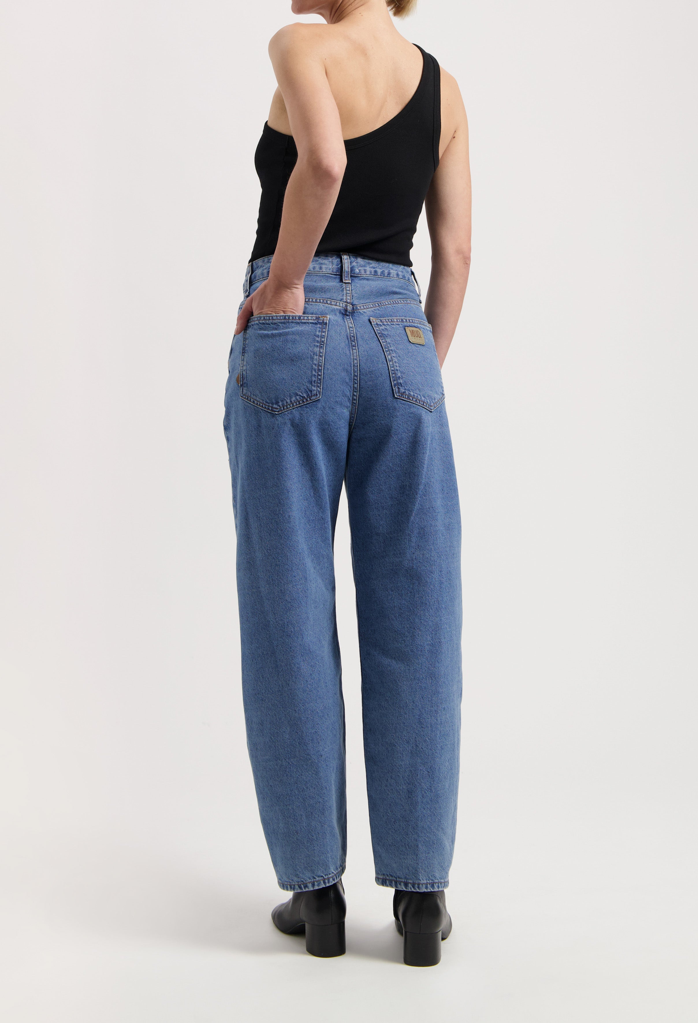 Woman wearing high-waisted blue denim jeans paired with a black one-shoulder top, showcasing a casual style.