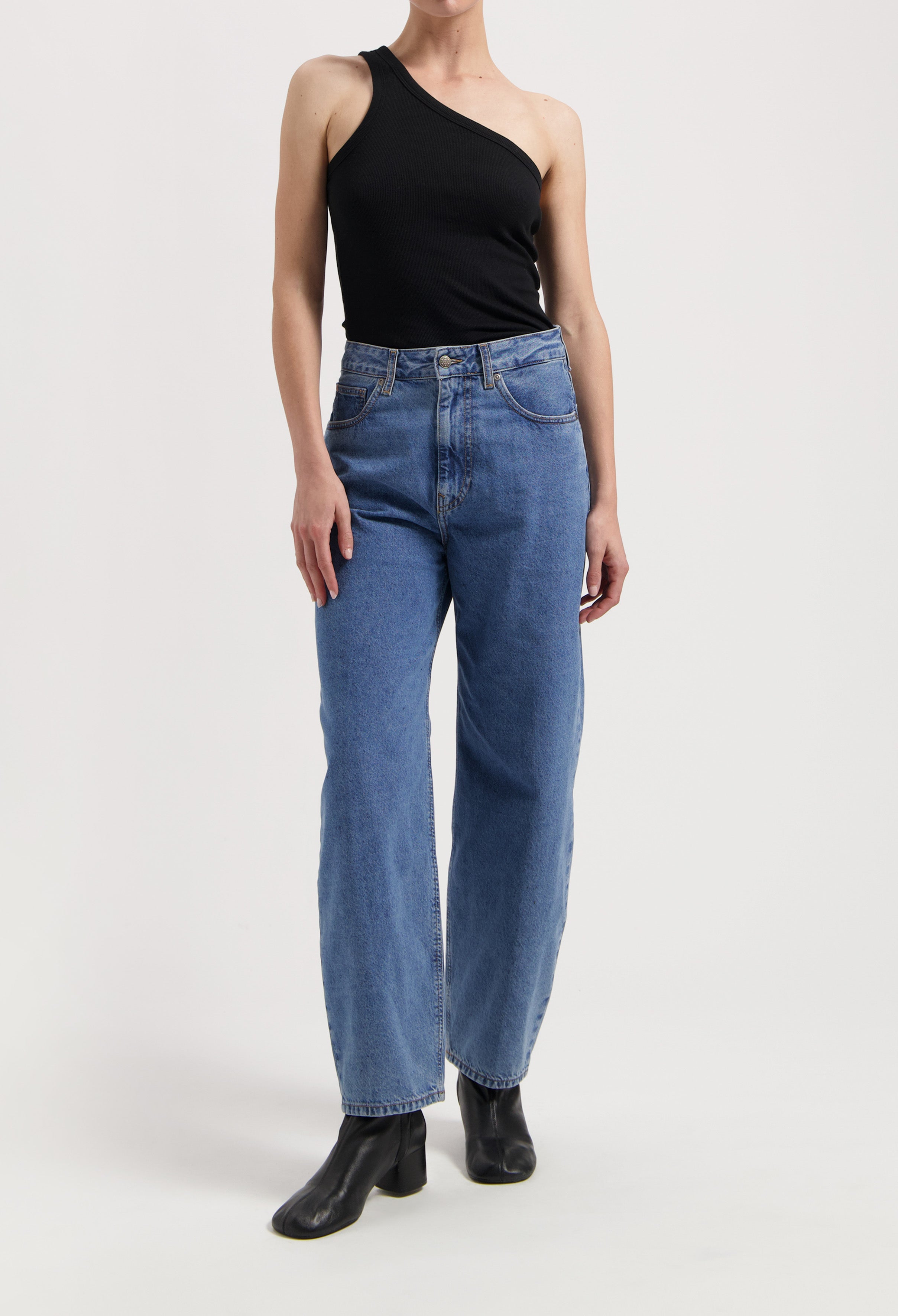 Wide-leg blue jeans paired with a black asymmetrical one-shoulder top and black ankle boots, showcasing casual style.