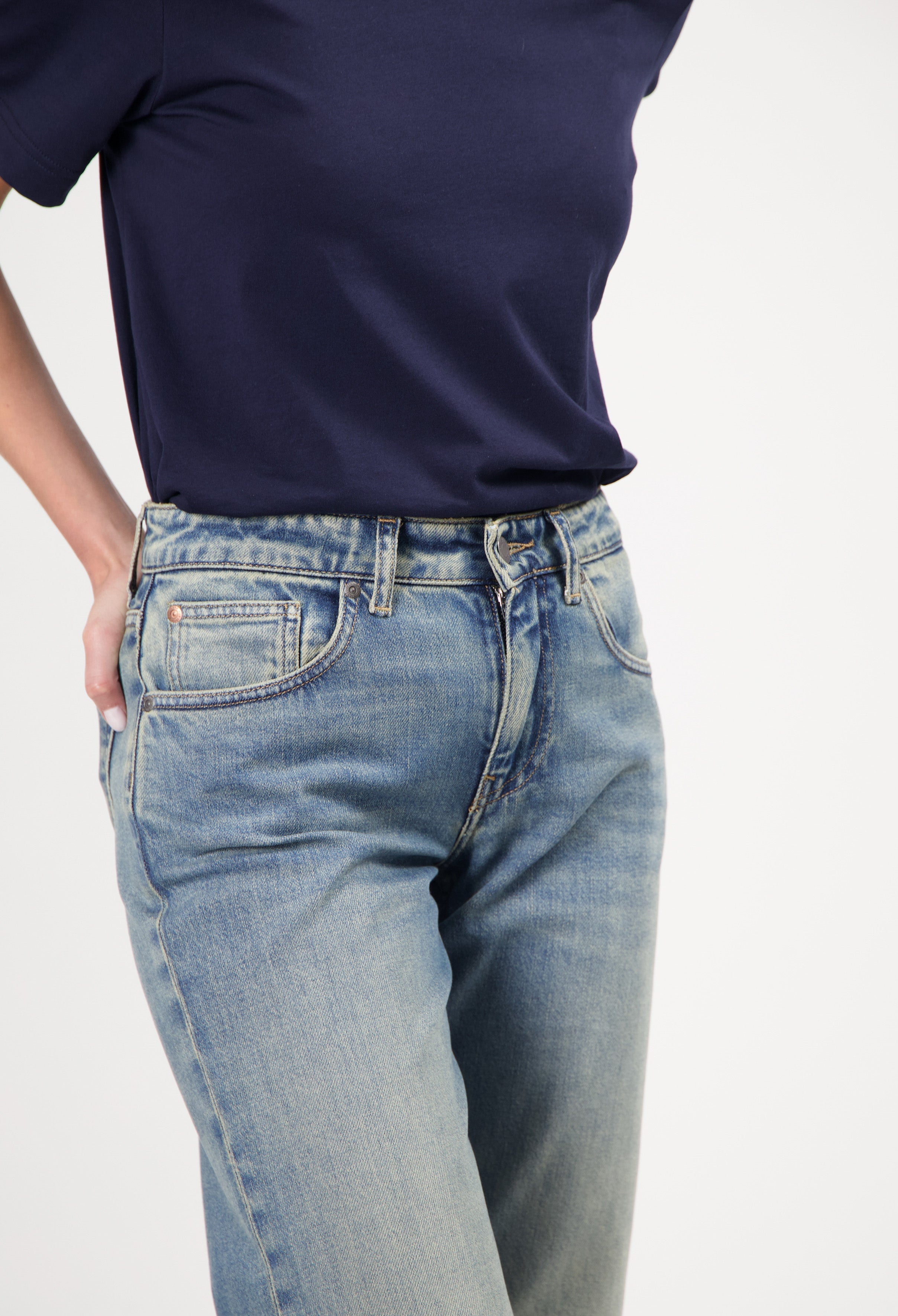 Model wearing classic light blue washed denim jeans with a navy blue short-sleeve top, hands in pockets.
