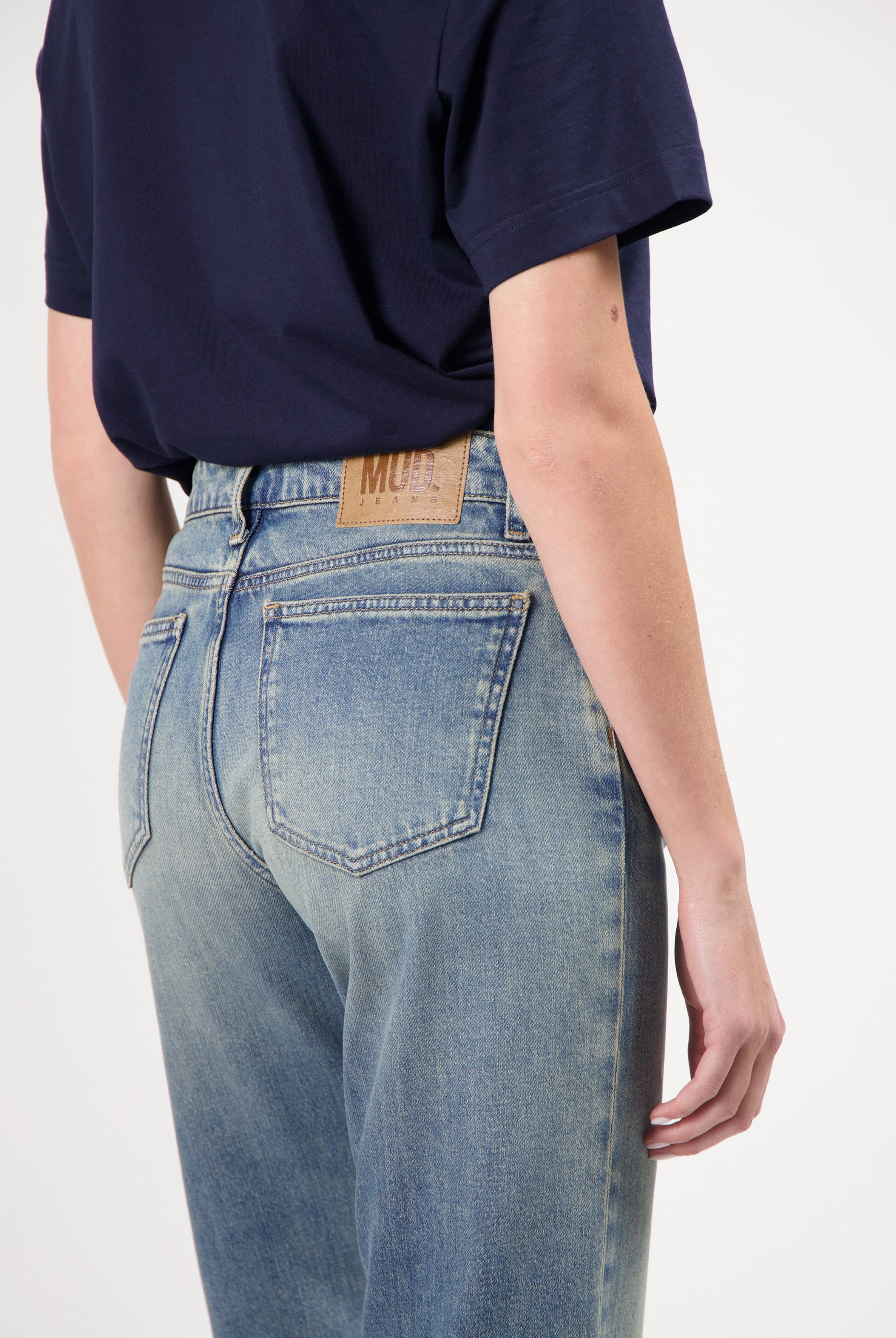 Person wearing light blue, eco-friendly MUD Jeans from organic cotton, displaying comfortable fit and stylish design.