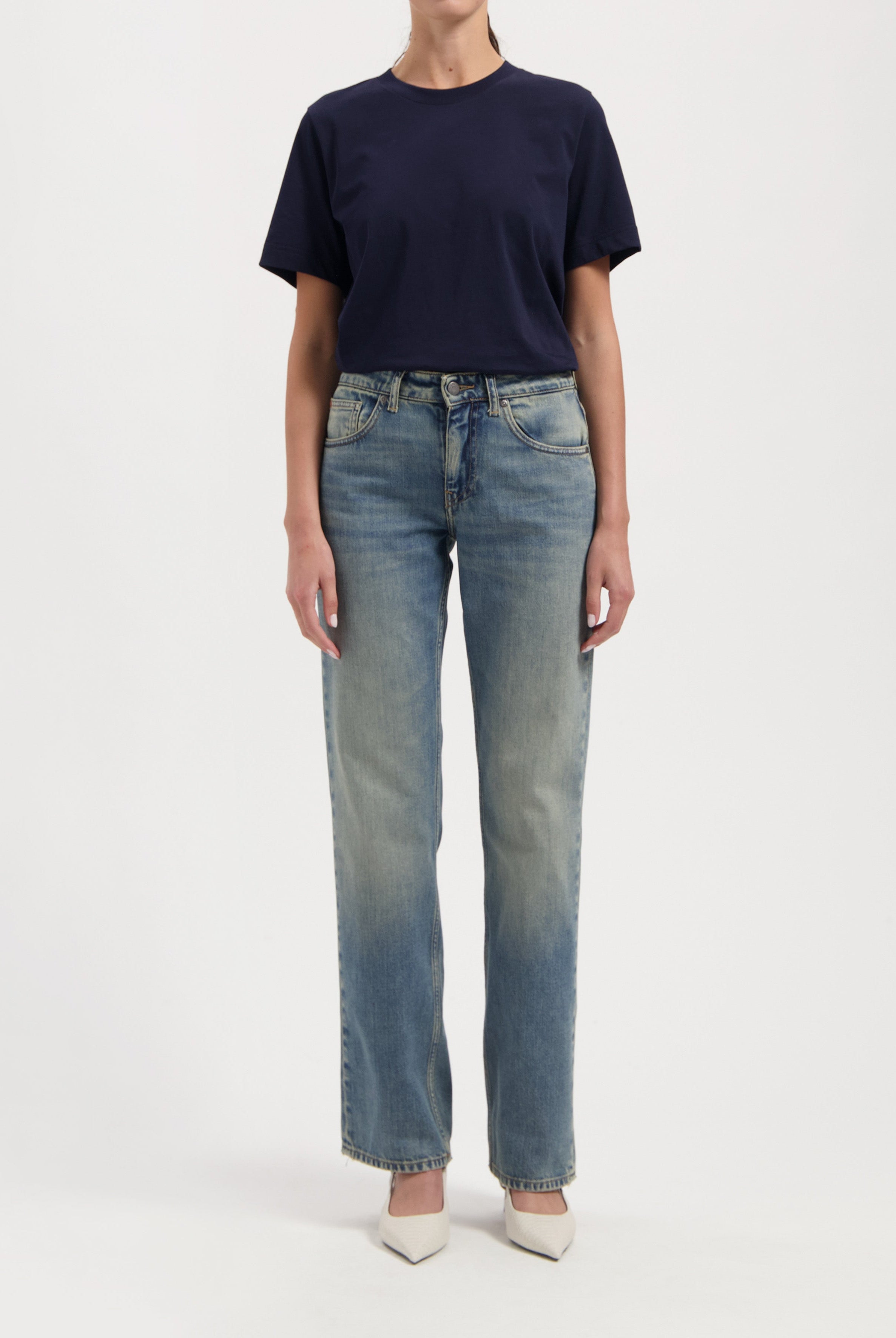 Casual outfit with a navy blue T-shirt paired with light-washed straight-leg jeans and white pointed-toe heels.