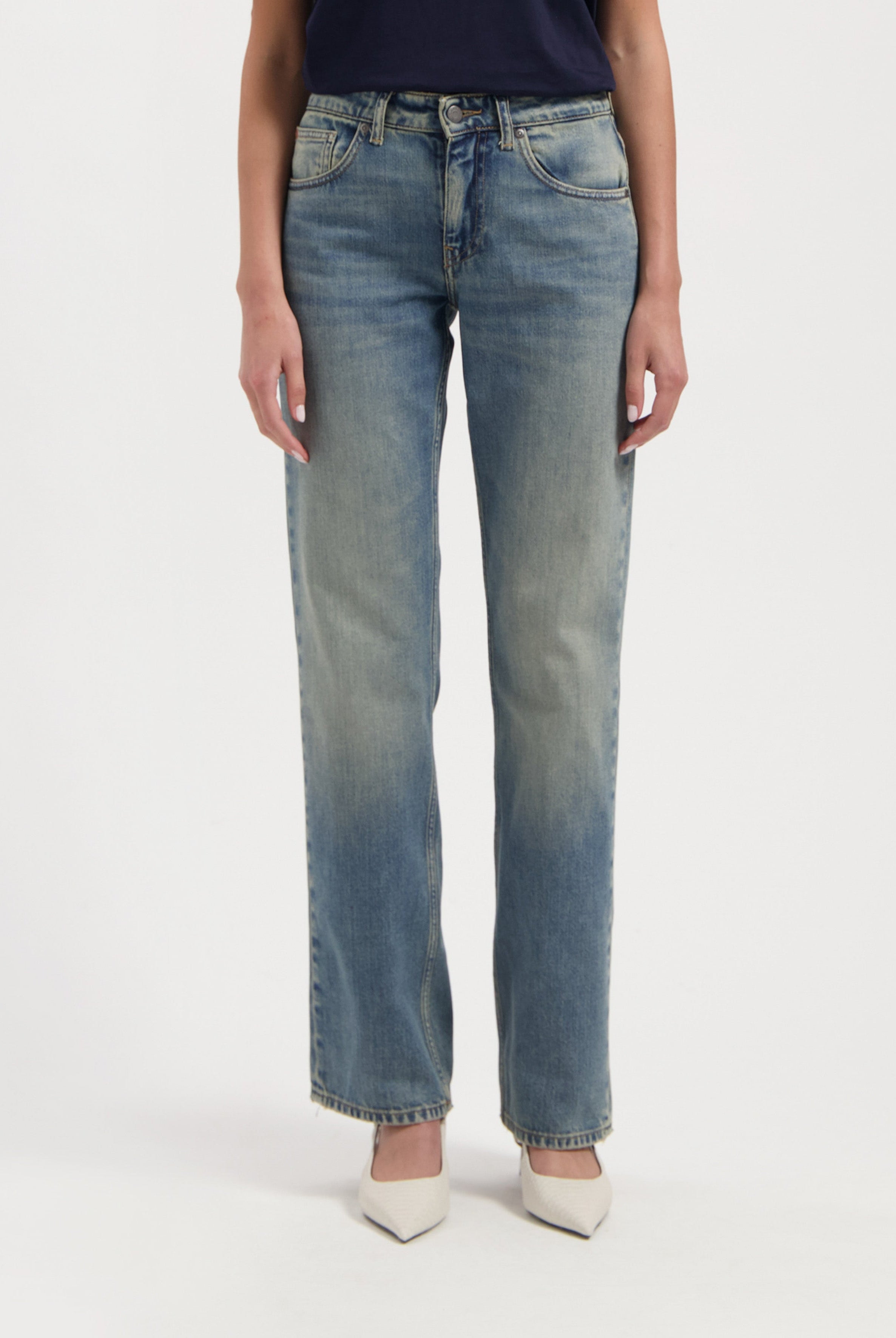 Light blue, straight-leg denim jeans made from cotton, worn with a dark navy top and white pointed-toe heels.