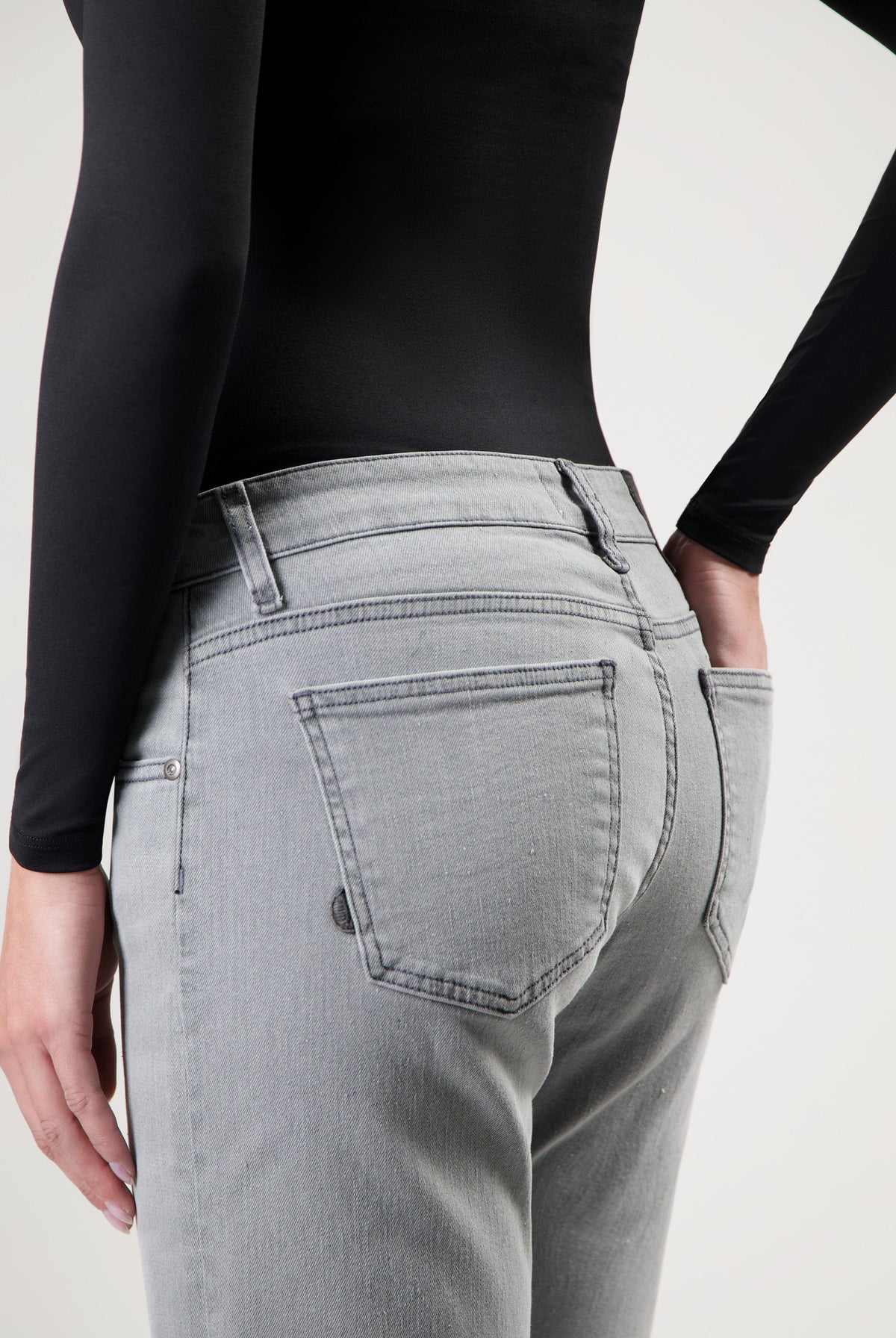 Person wearing light gray jeans with back pockets, styled with a black long-sleeve top, showcasing casual fashion.