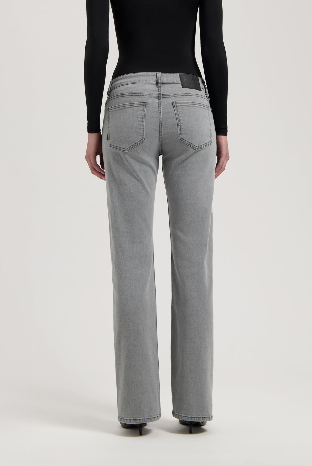 Gray high-waisted denim jeans with straight-leg fit, featuring detailed stitching and worn with a black long-sleeve top.