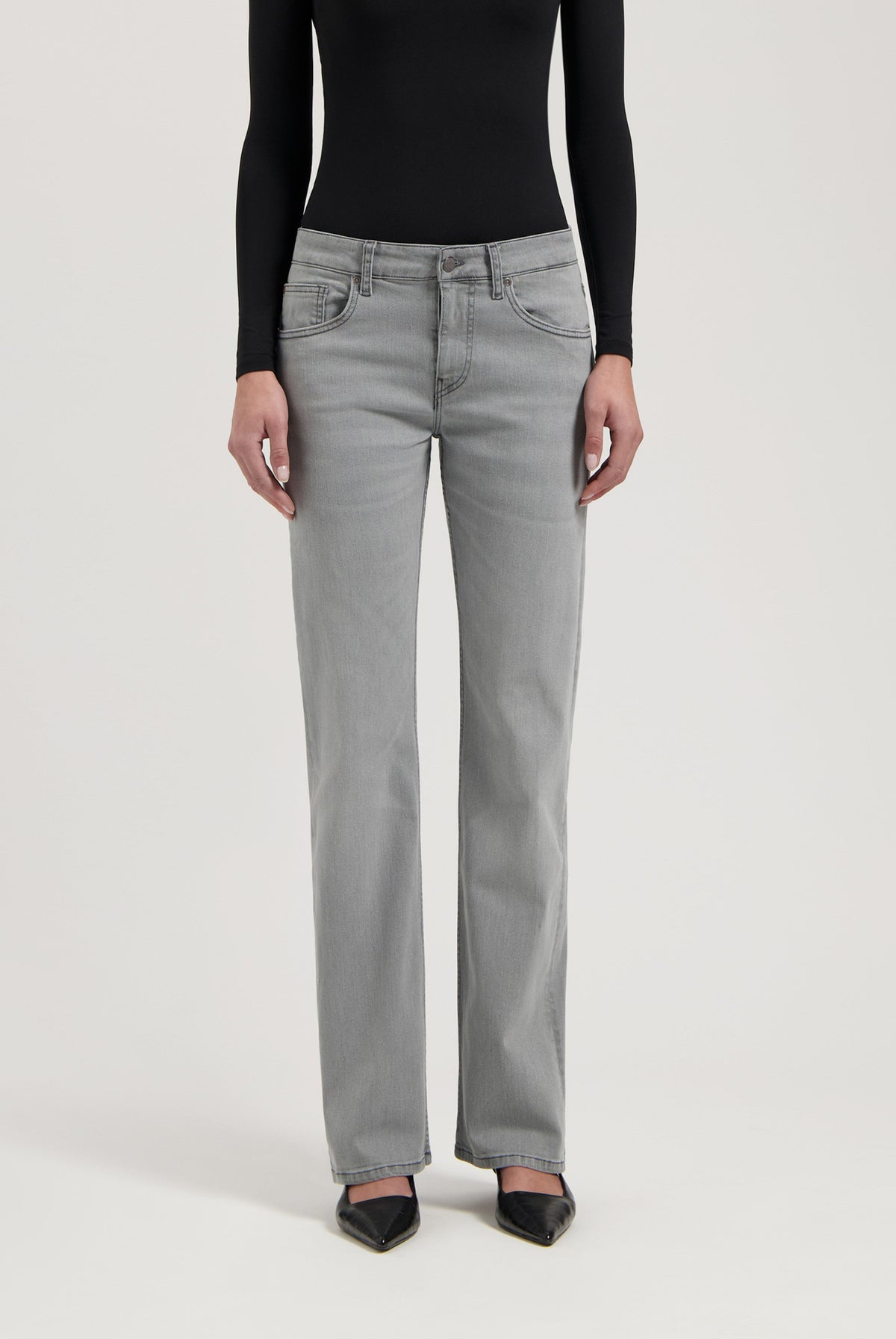 Gray straight-leg jeans paired with a sleek black long-sleeve top and pointed black heels for a modern look.