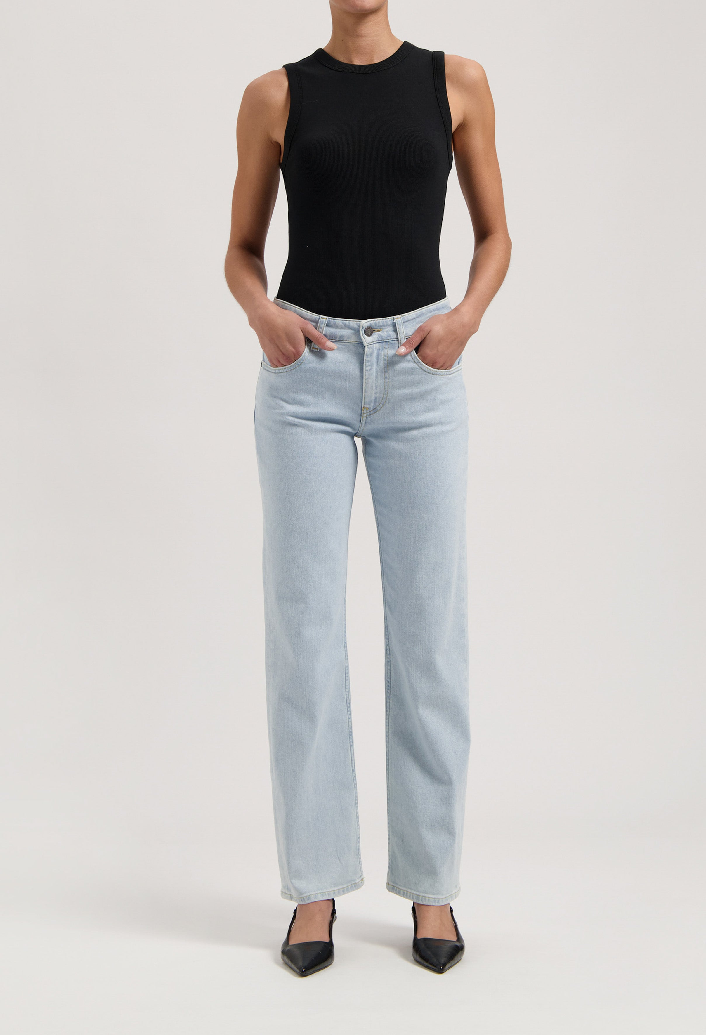 Light blue, straight-leg jeans paired with a fitted black sleeveless top and black pointed-toe heels.