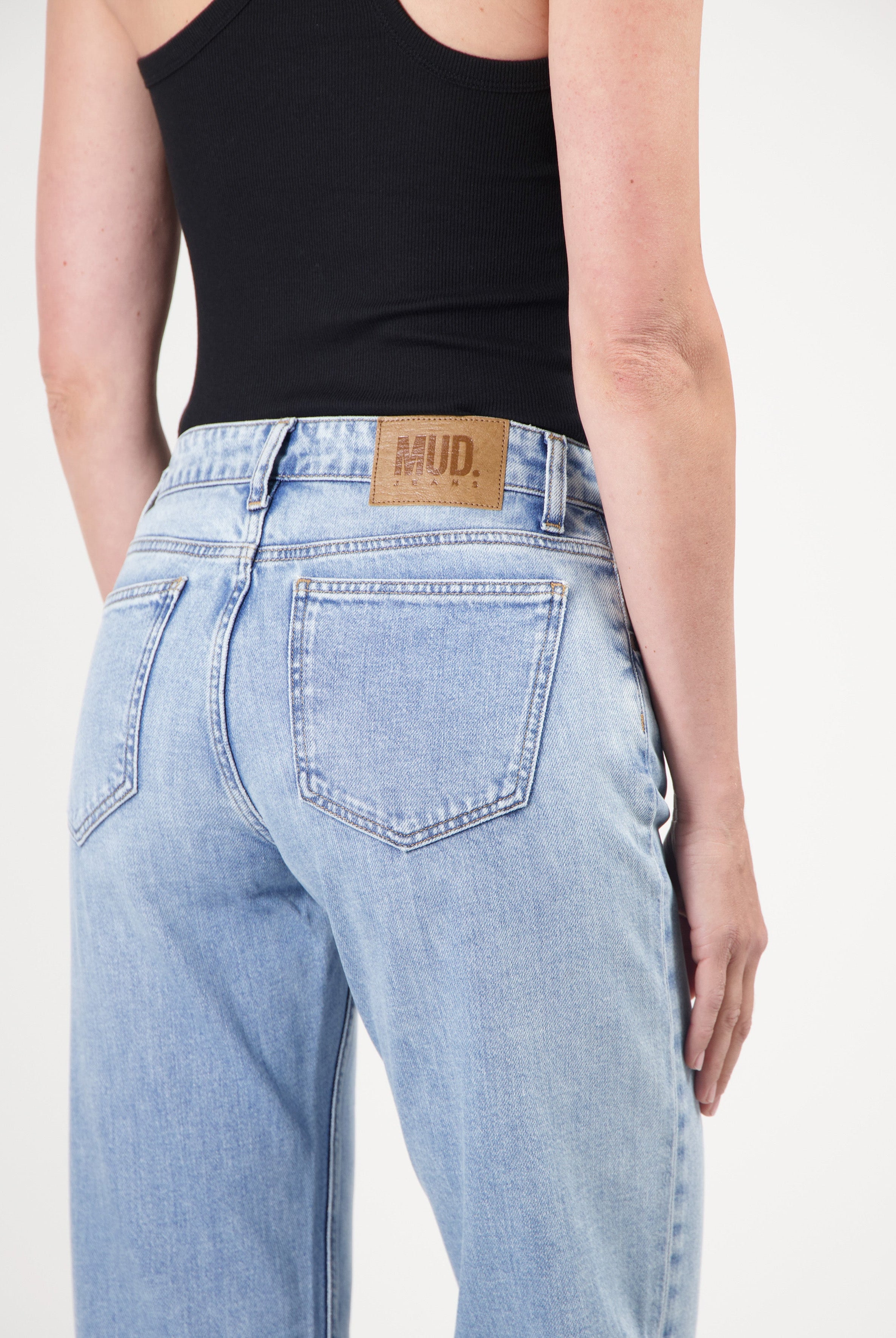 Eco-friendly MUD Jeans in light blue organic denim, featuring a high-waist fit, worn with a black sleeveless top.