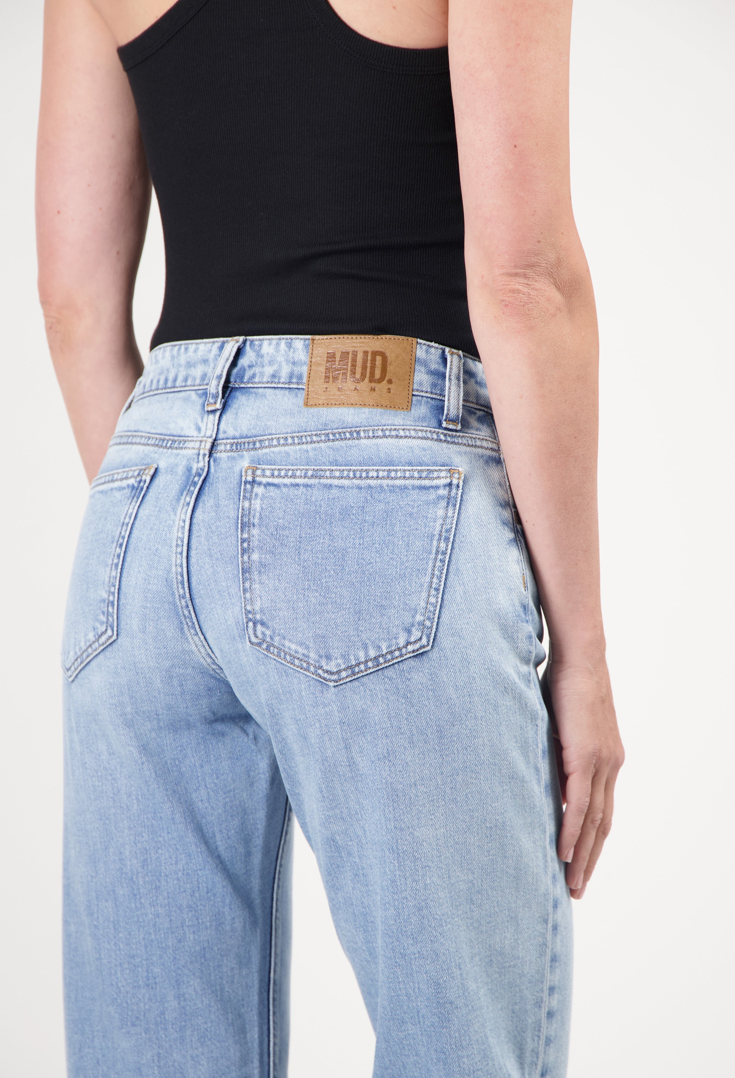 Eco-friendly MUD Jeans in light blue organic denim, featuring a high-waist fit, worn with a black sleeveless top.
