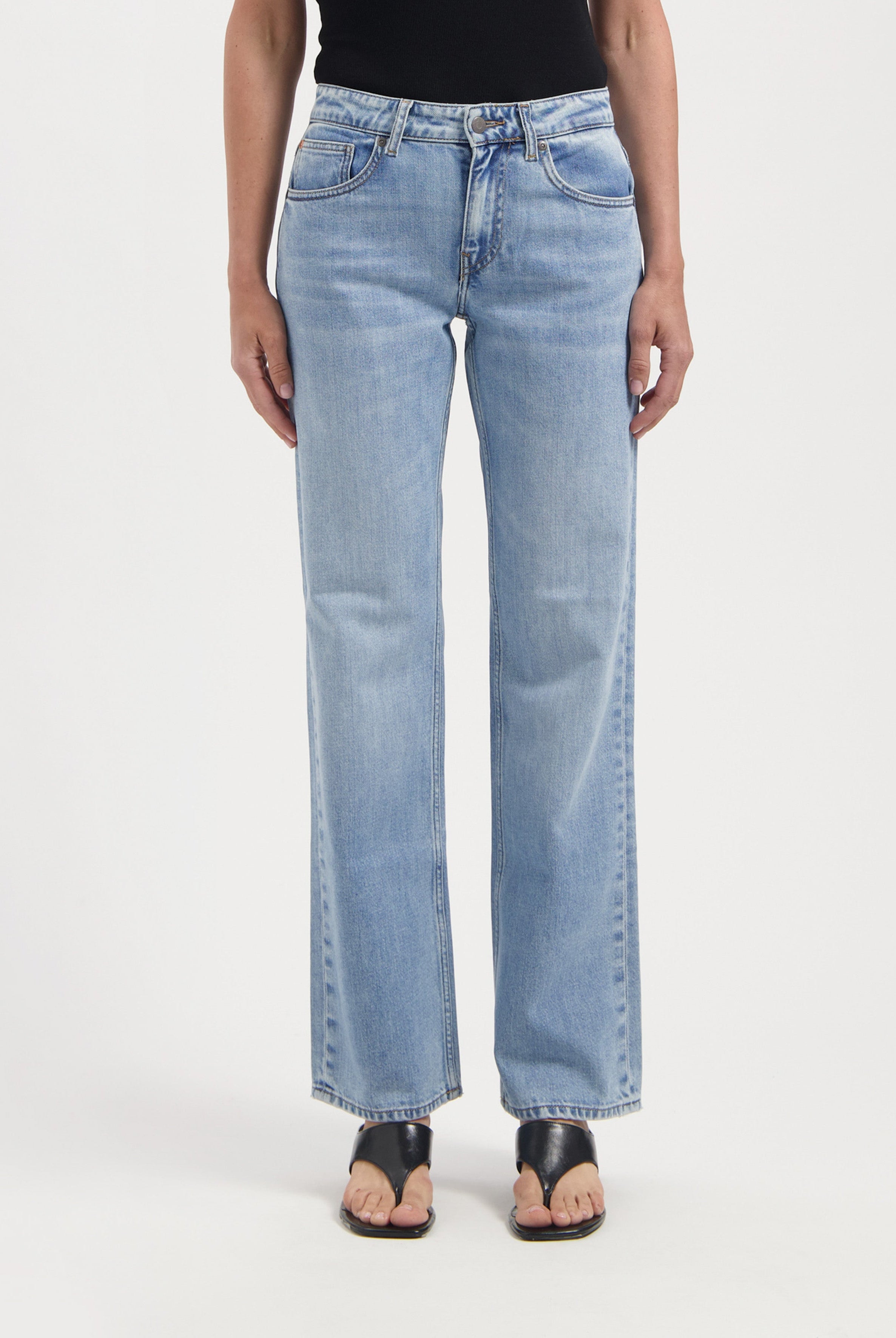 Light blue straight-leg jeans made from denim, worn with a black top and open-toe black sandals on a white background.