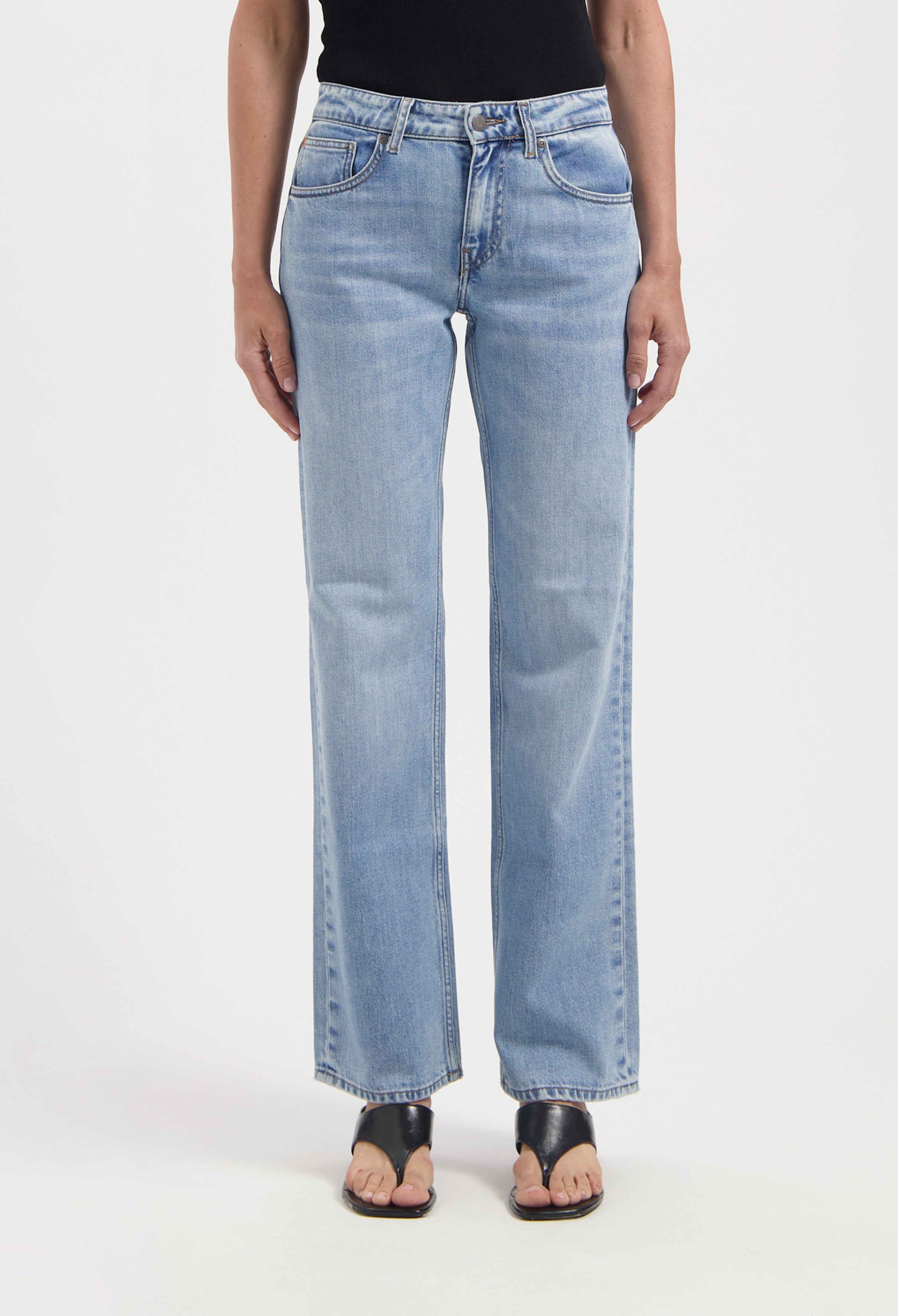 Light blue straight-leg jeans made from denim, worn with a black top and open-toe black sandals on a white background.
