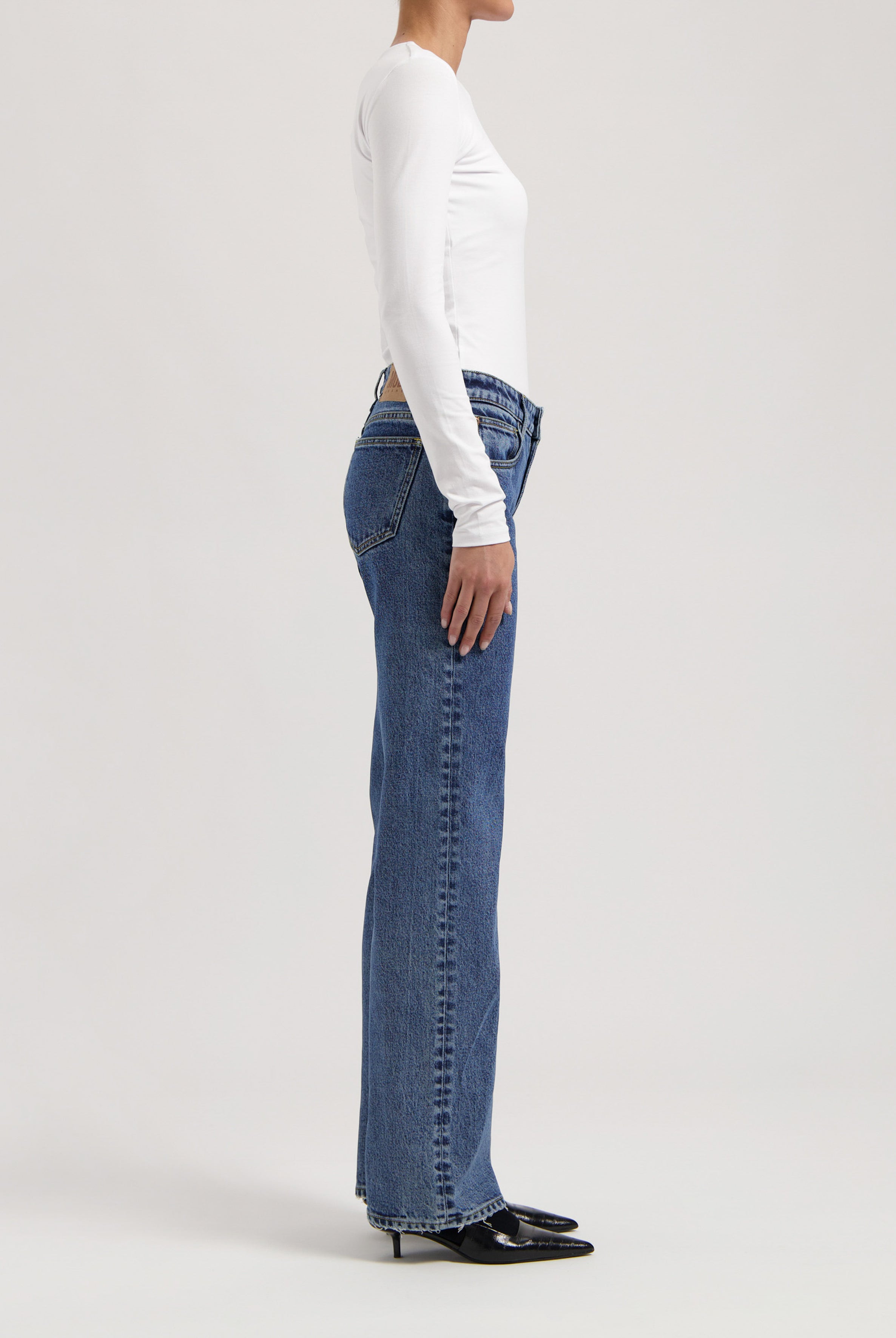 Side profile of a person wearing classic blue straight-leg jeans paired with a fitted white long-sleeve top and black heels.