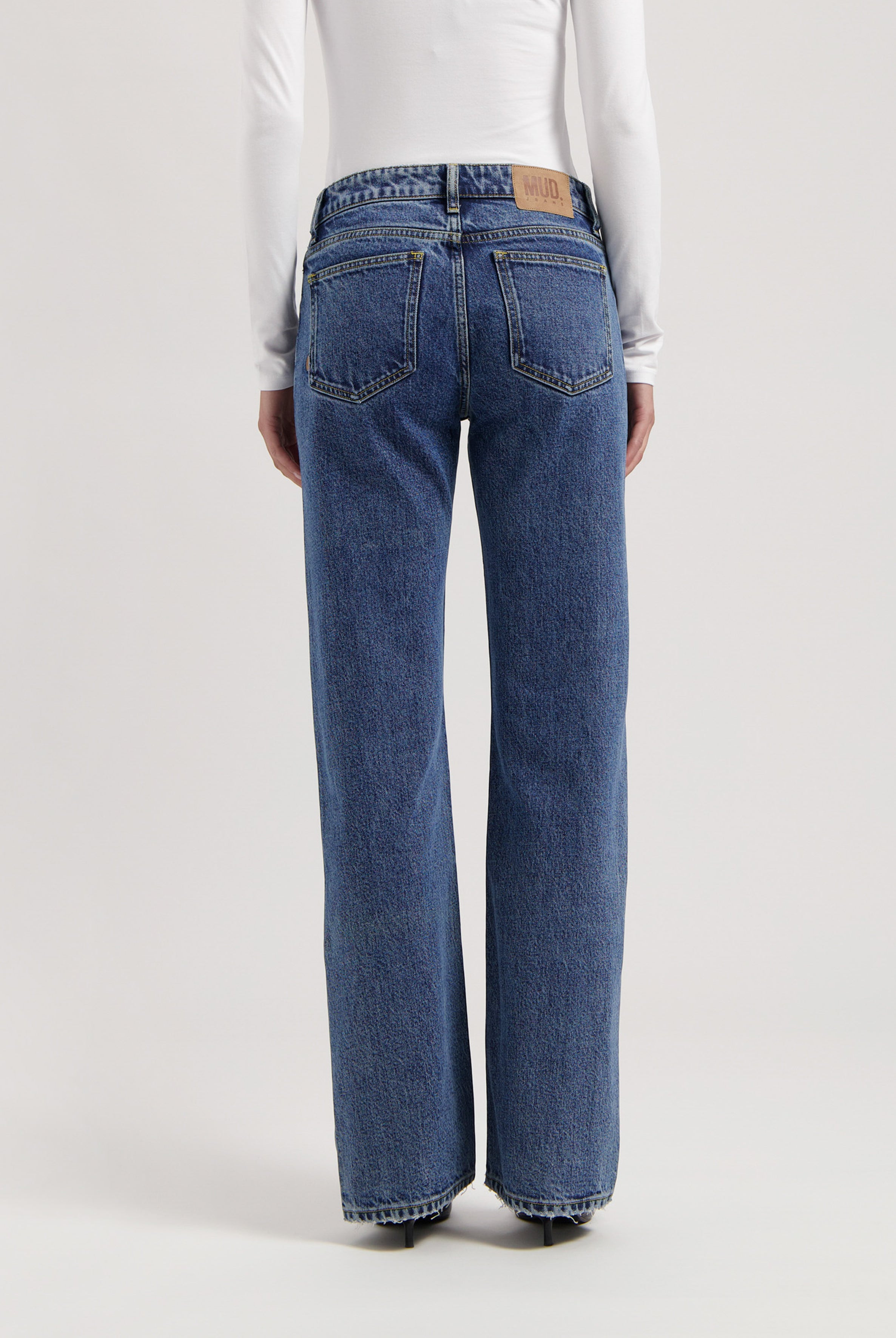 Back view of classic blue straight-leg denim jeans with a high waistband, worn with a long-sleeve white top.